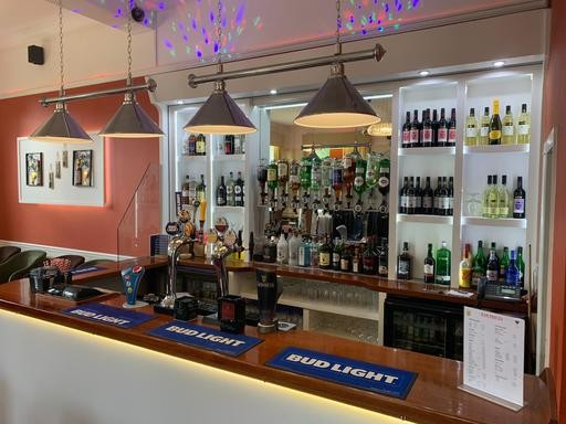 Bar area with hanging pendant lights, bottles of wine and spirits on shelves, beer taps with Bud Light mats on the counter, and some decorative lights on the ceiling.