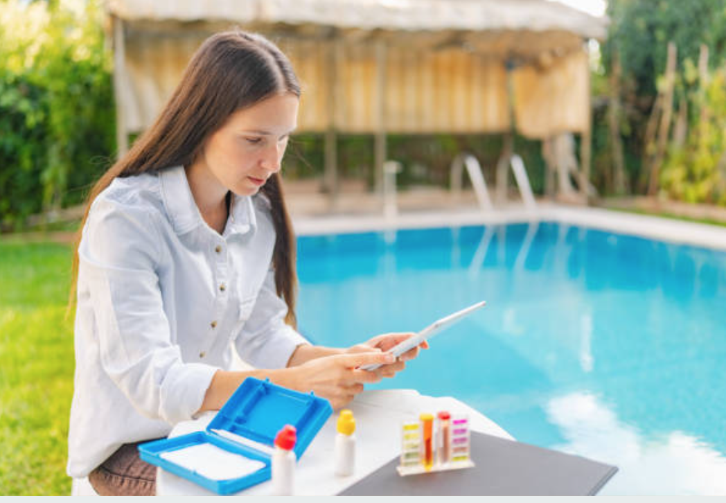 Woman sitting by a swimming pool, preparing to test water with testing kit.