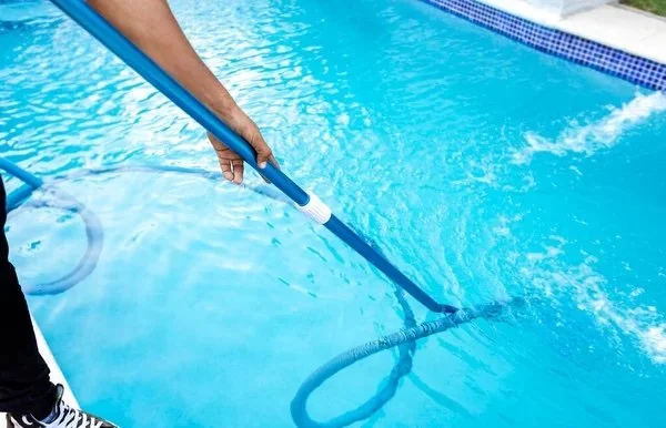 Person cleaning a swimming pool with a telescopic pole and net