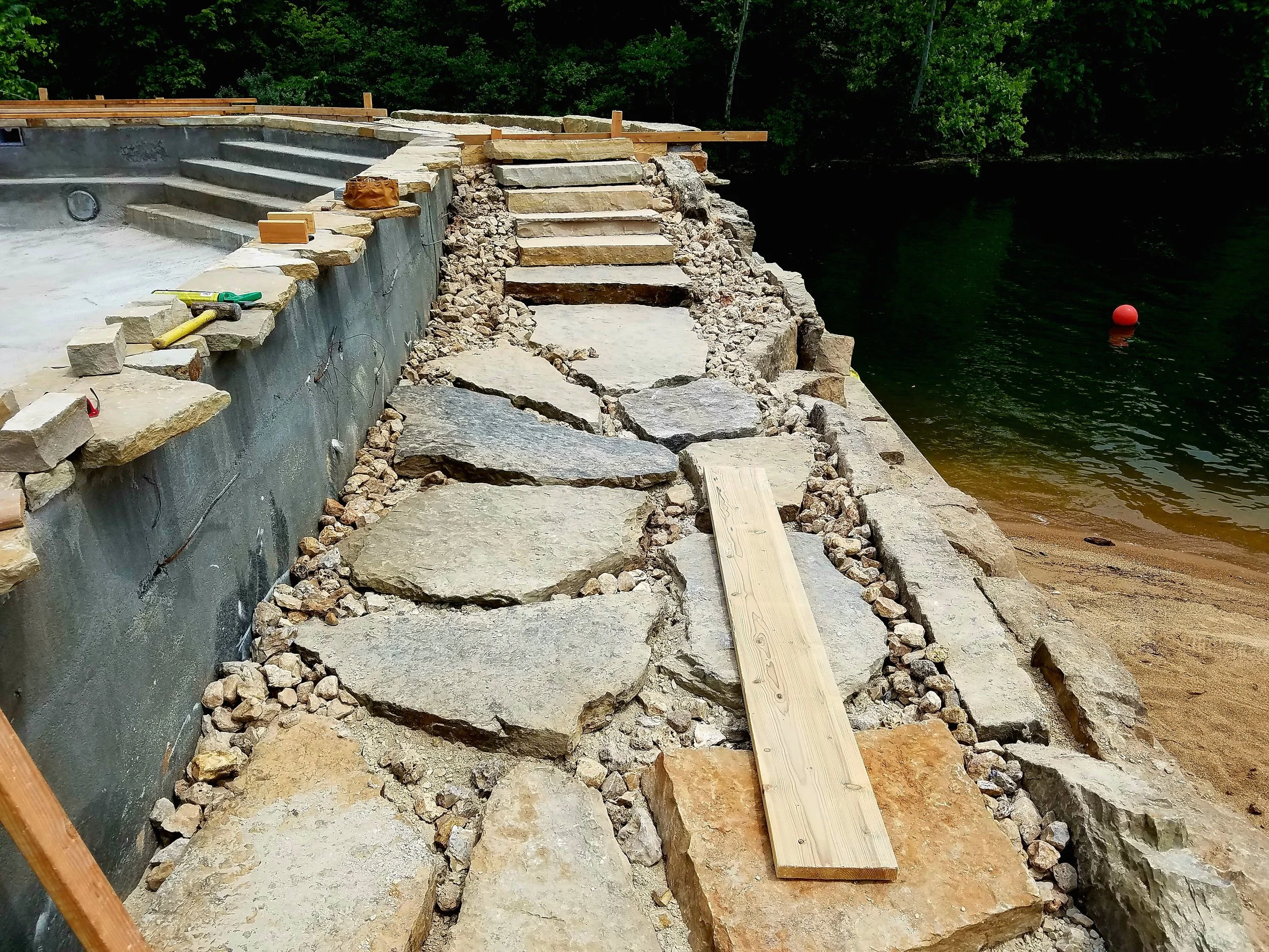 Construction of a stone pathway along a lakeshore with stairs and construction tools visible.