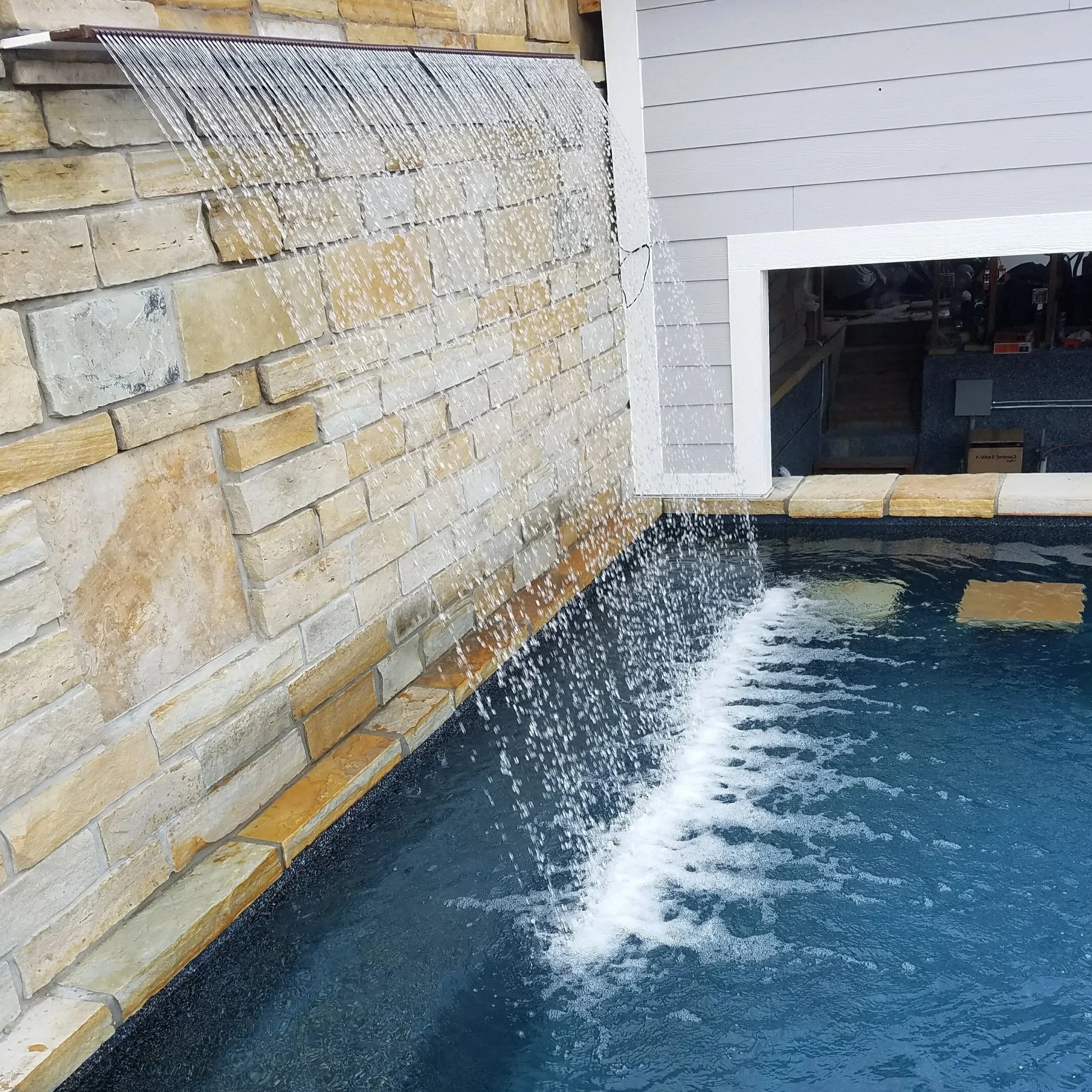 Water feature with waterfall spilling over a brick wall into a pool.