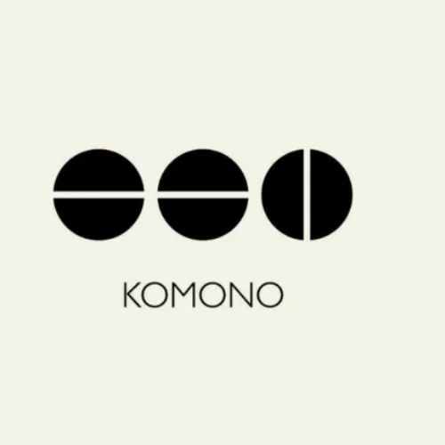 Logo minimaliste avec trois cercles noires, chacun divisé par une ligne ou une moitié, avec le texte 'KOMONO' en dessous