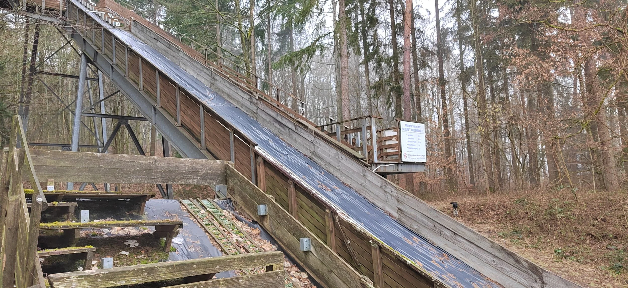 Schlittenbahn im Wald, mit Holz- und Metallstrukturen, das Wetter ist bewölkt, im Hintergrund Bäume.
