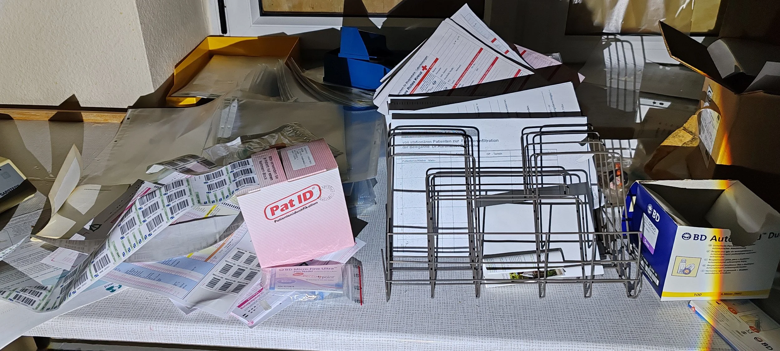 Ein Tisch mit medizinischen Dokumenten, Proben, einem Pat-Identifikationsschild, Medikamentenverpackungen und einem Metallkorb.