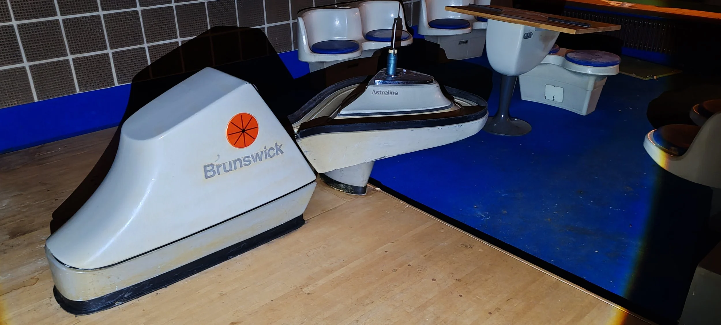 Ein altes Luftgewehr-Spielsystem mit der Aufschrift 'Brunswick' und 'Astraline' im Spielsaal, das früher für Unterhaltungszwecke genutzt wurde. Es ist auf einem Holztisch platziert, umgeben von Sitzbänken und weiteren Spielgeräten.