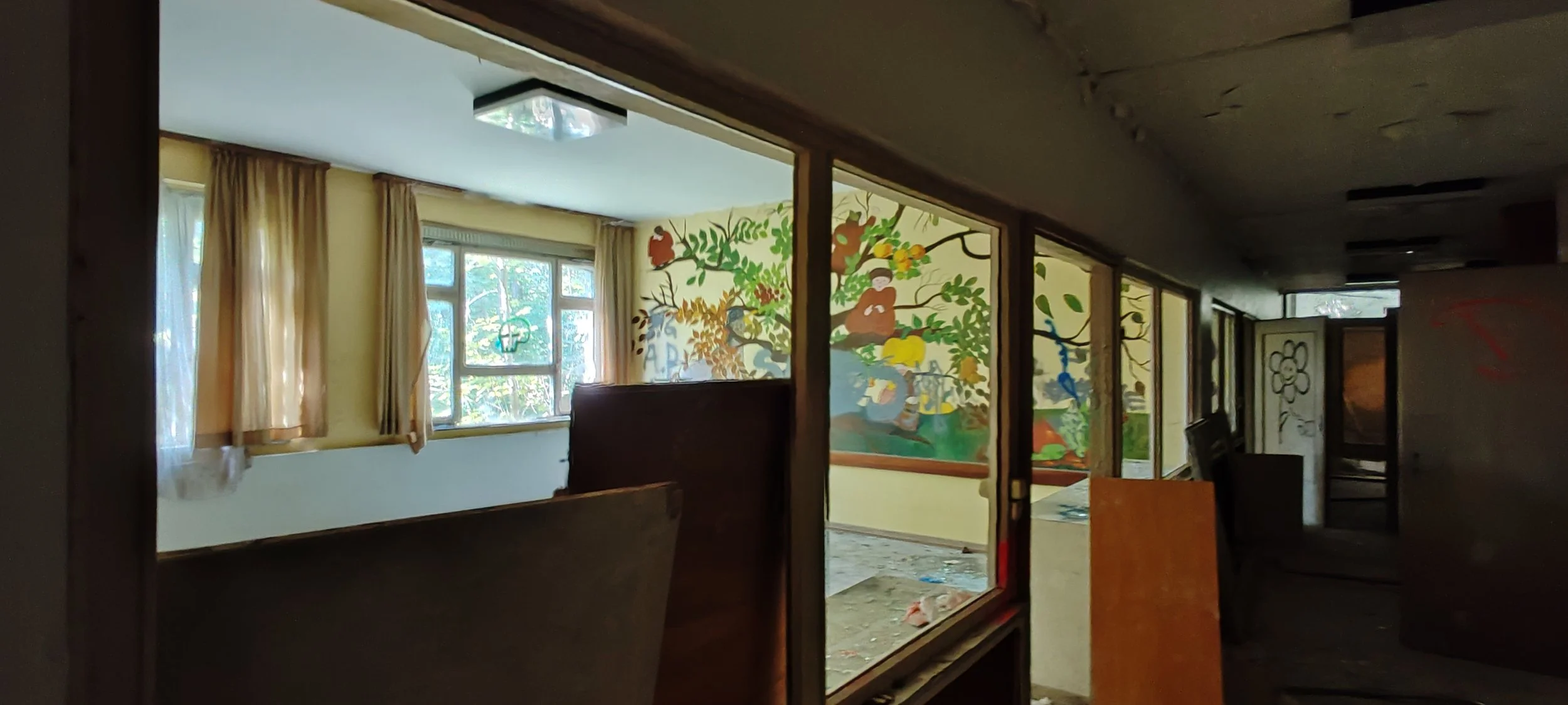 Abgelegenes, verlassenes Zimmer mit zerbrochenen Fenstern, einem Wandbild eines Affen im Baum und verpfäffter Einrichtung.