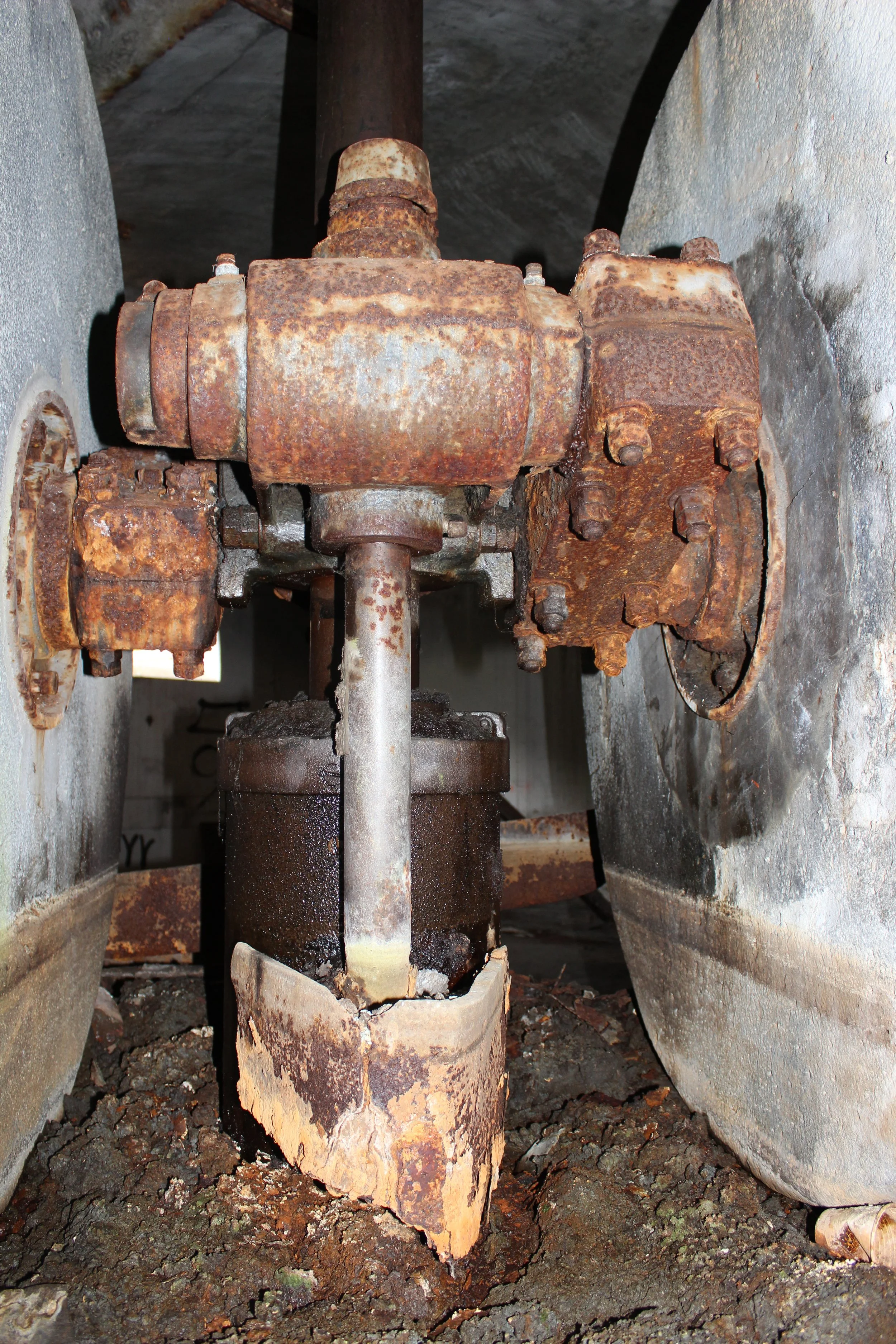 Ein verrosteter, alter Mechanismus zwischen zwei Betonwänden, vermutlich Teil einer Industrieanlage oder eines alten Geräts.