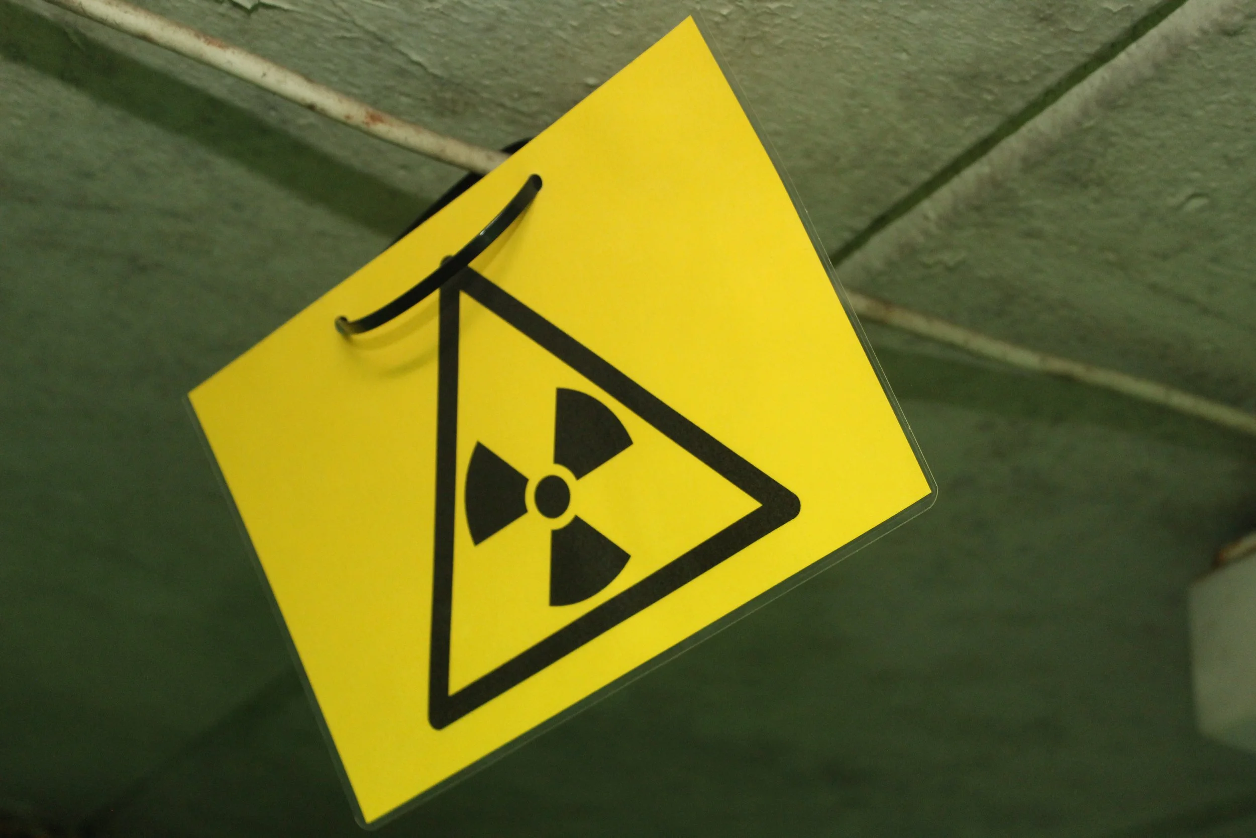 Gelbes Schild mit einem schwarzen radioaktiven Symbol, an der Wand befestigt.