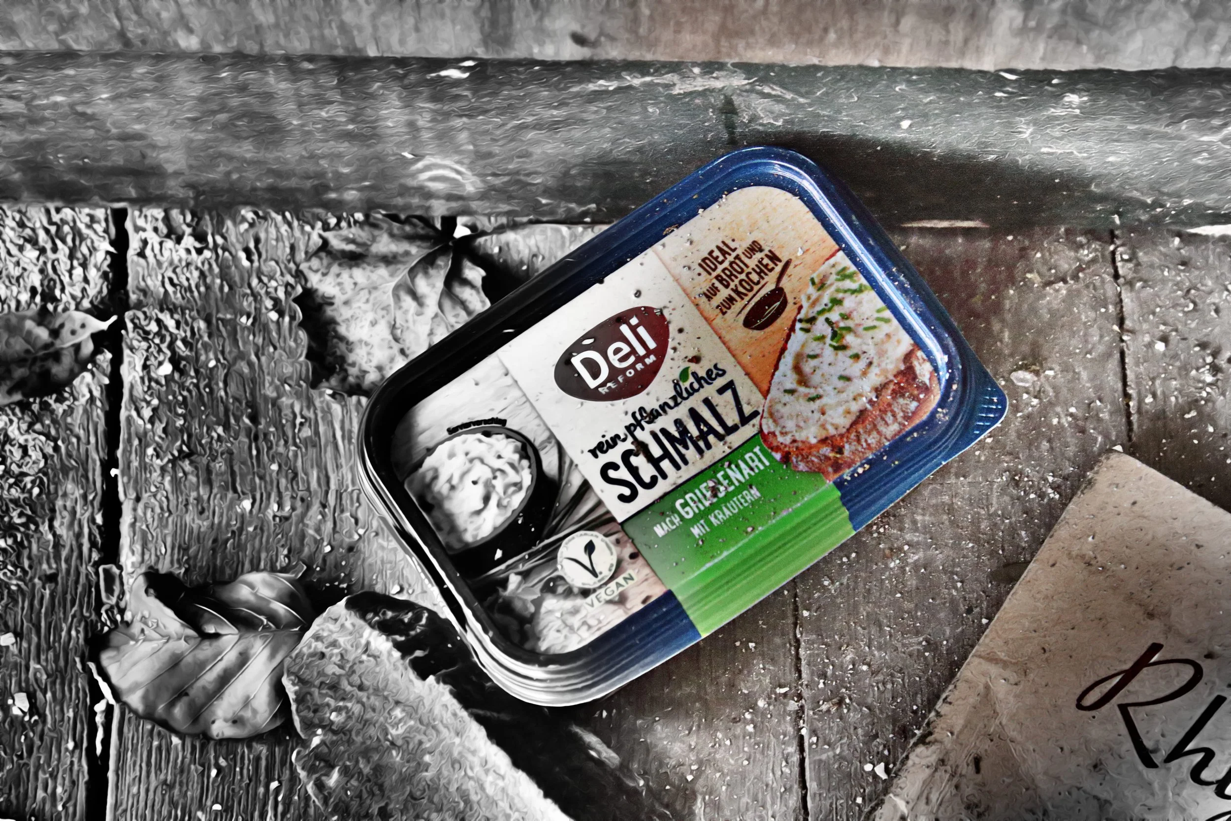 Ein Becher vegane pflanzliche Quarkalternative mit Kräutern auf einem rustikalen Holzoberfläche neben einem weißen Blatt Papier.