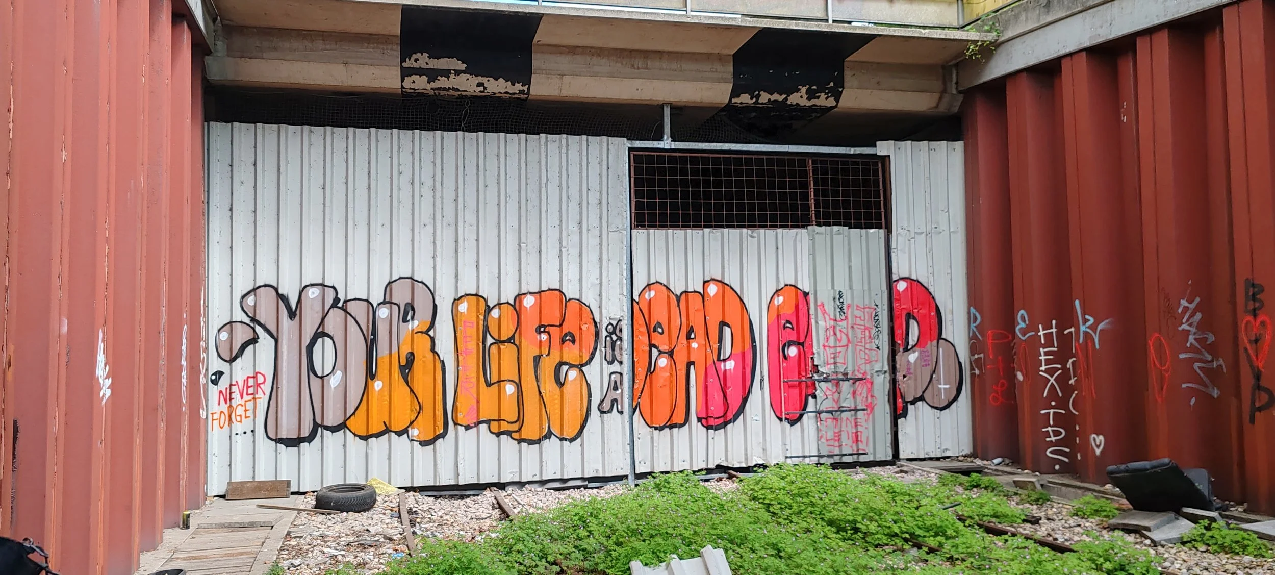 Graffiti auf einer Metalltür mit den Worten 'YOU'RE DEAD' in großen bunten Buchstaben, darunter kleinere Graffiti und der Text 'NEVER FORGET' auf der linken Seite.