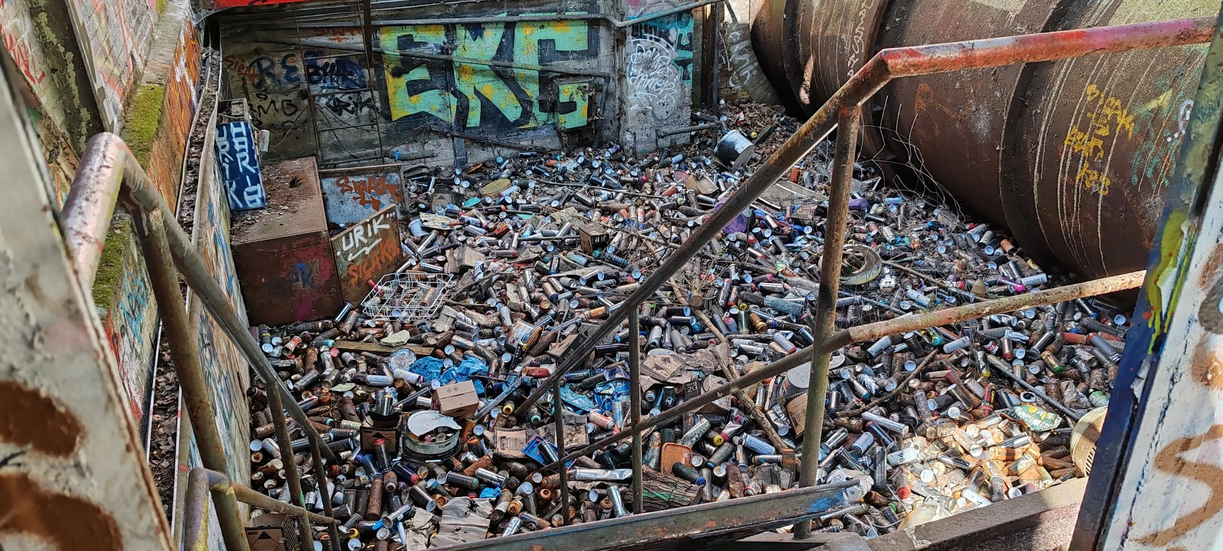 Abandoned, graffiti-decorated Urban Scene, voll mit leeren Spraydosen und Müll, mit rostigen Metallstrukturen.