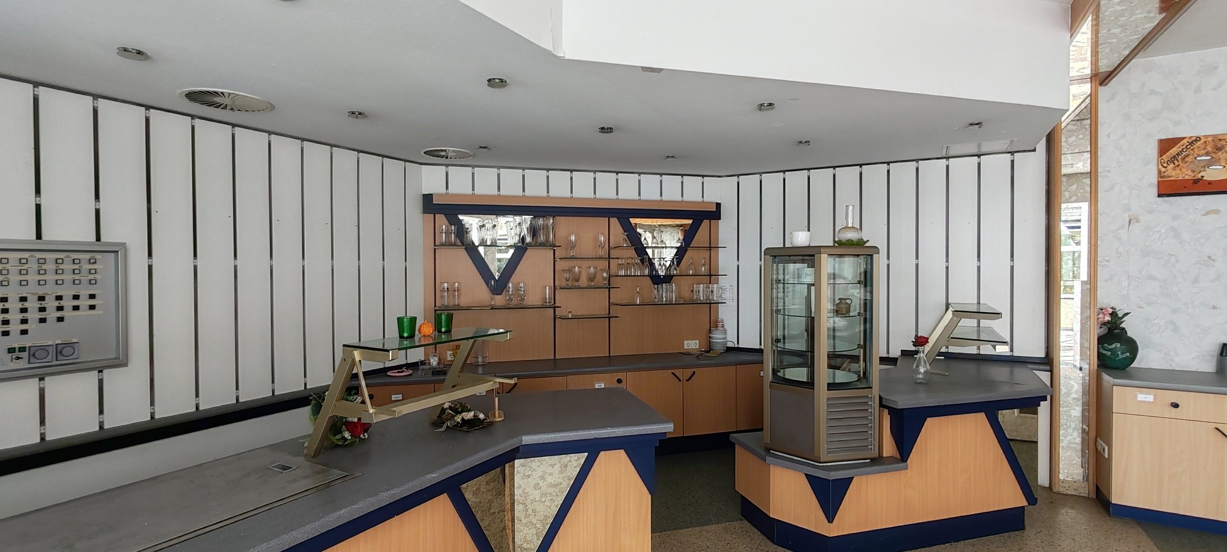 Innenraum eines Cafés oder Restaurants mit Theke, Gläsern und Dekorationsgegenständen.