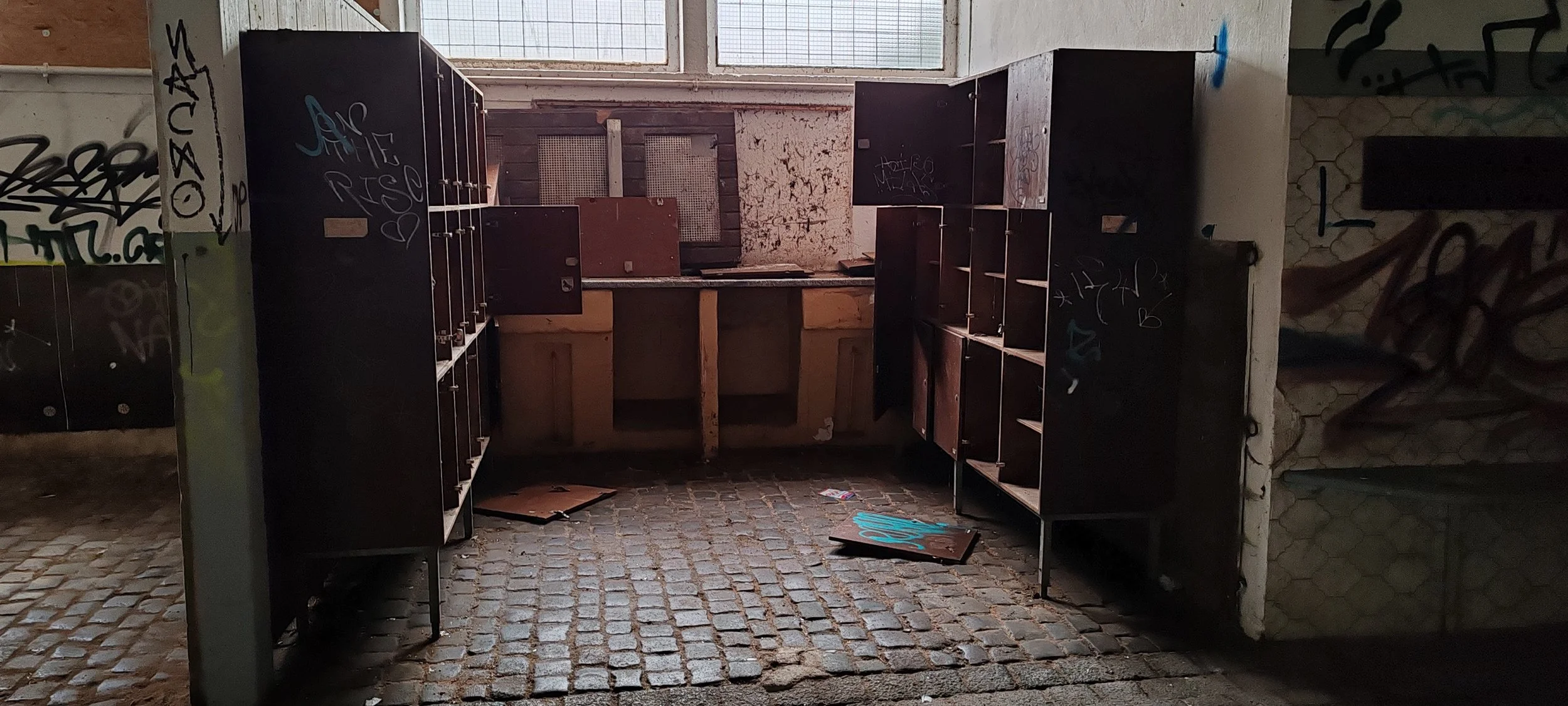 Verlassener, verunstalteter Raum mit zerbrochenen Schubladen, Graffiti an den Wänden und einem unordentlichen, mit Steinen gepflasterten Boden.