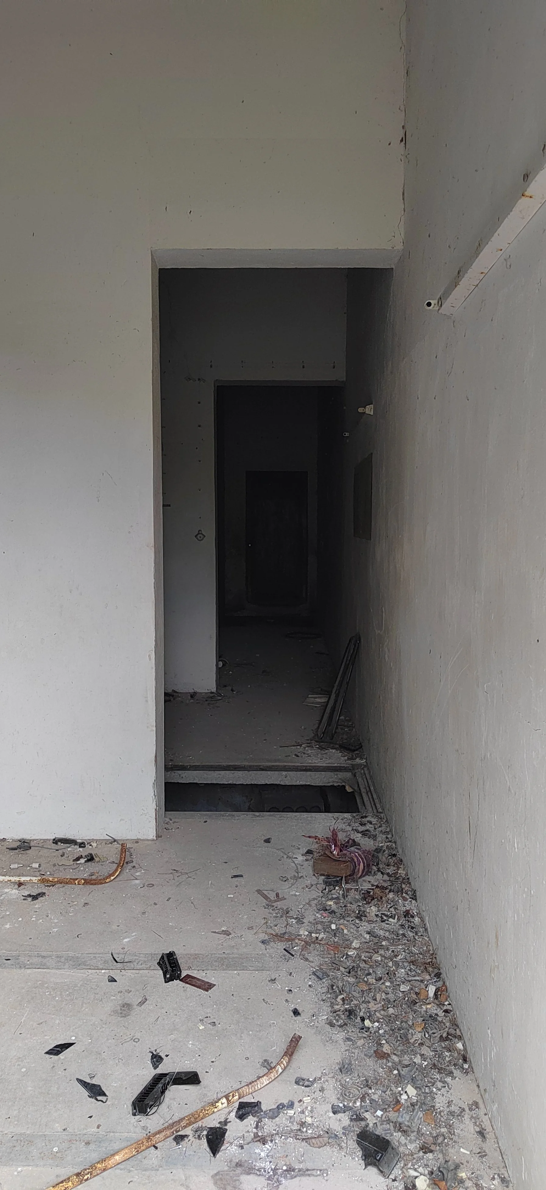 Innenansicht eines unvollendeten, staubigen Gebäudes mit offenen Kabeln und zerbrochenem Baumaterial auf dem Boden, eine Treppe führt nach unten.