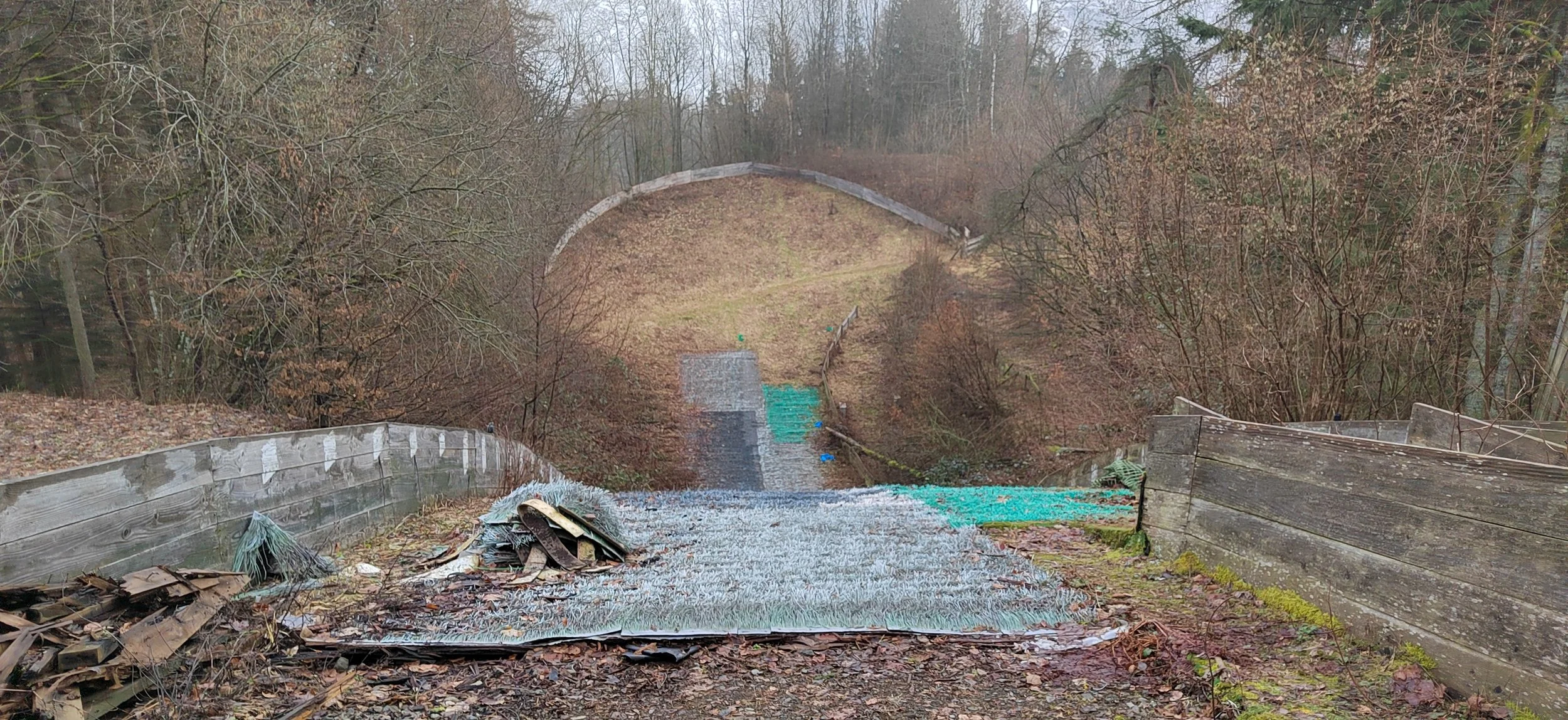 Verlassene, beschädigte Brücke im Wald, mit zerbrochenem Glas und Holzresten, umgeben von toten Blättern und kahlen Bäumen.