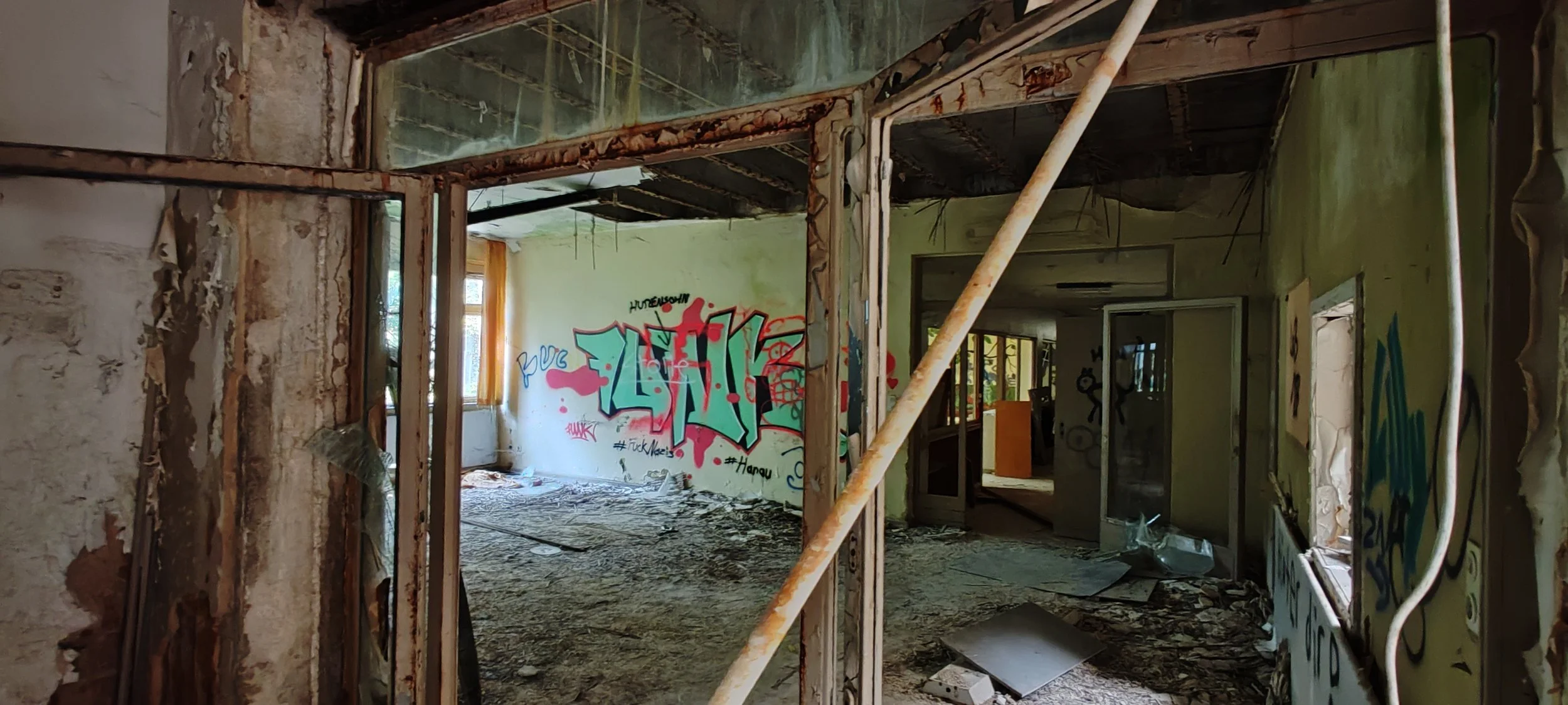 Innenansicht eines verfallenen Gebäudes mit zerbrochenen Wänden, Graffiti an den Wänden und herumliegenden Trümmern am Boden.