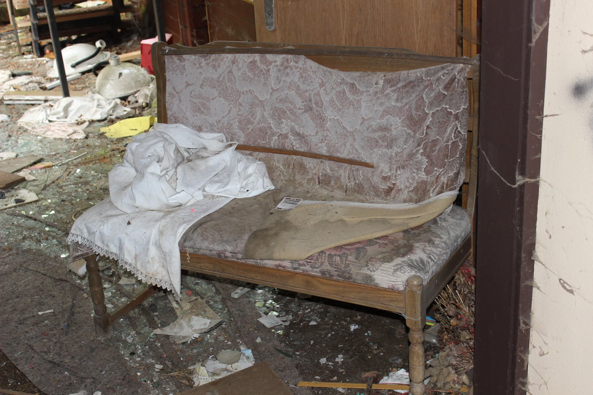 Verunreinigte, alte Couch in einem zerfallenen Raum, umgeben von Müll und Schmutz.