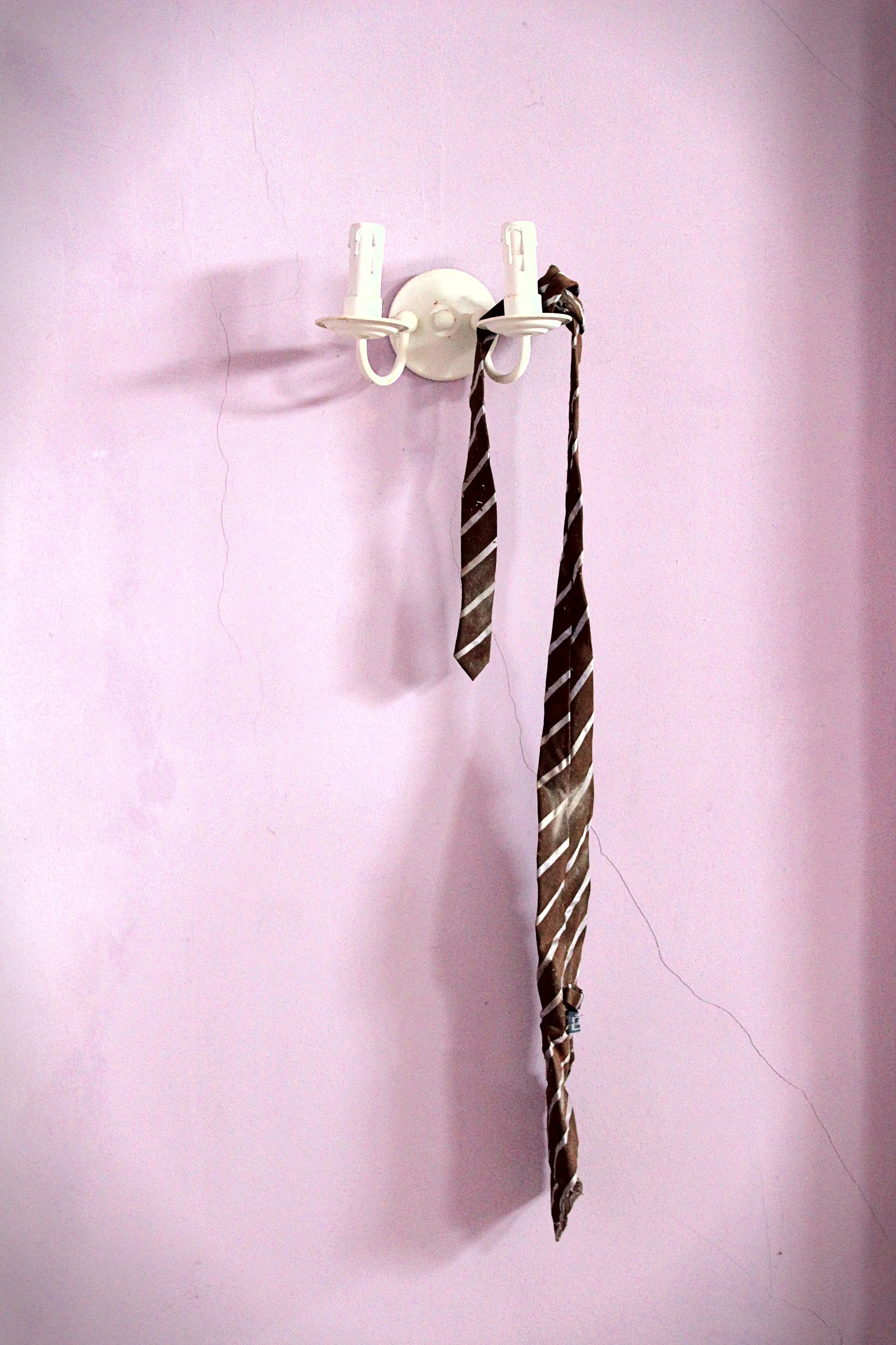 Ein rosa Wand mit einer weißen Kleiderhaken, an der ein dunkler Krawatte hängt.