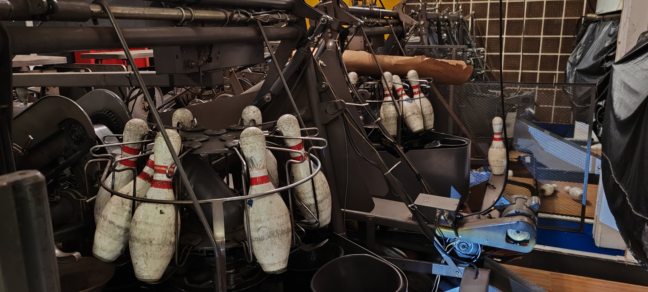 Nutzlose Bowlingkugeln und - Pins in einer Werkstatt, umgeben von technischen Geräten und Drähten.