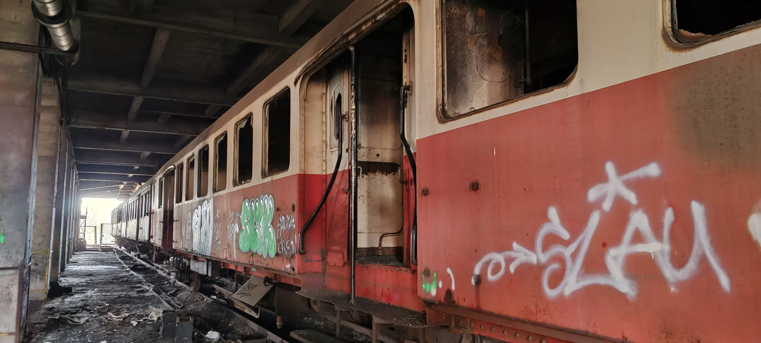 Verfallener, graffiti-übersäter Zug in einer abgedeckten, dunklen Lagerhalle, mit vorbeigehendem Licht im Hintergrund.