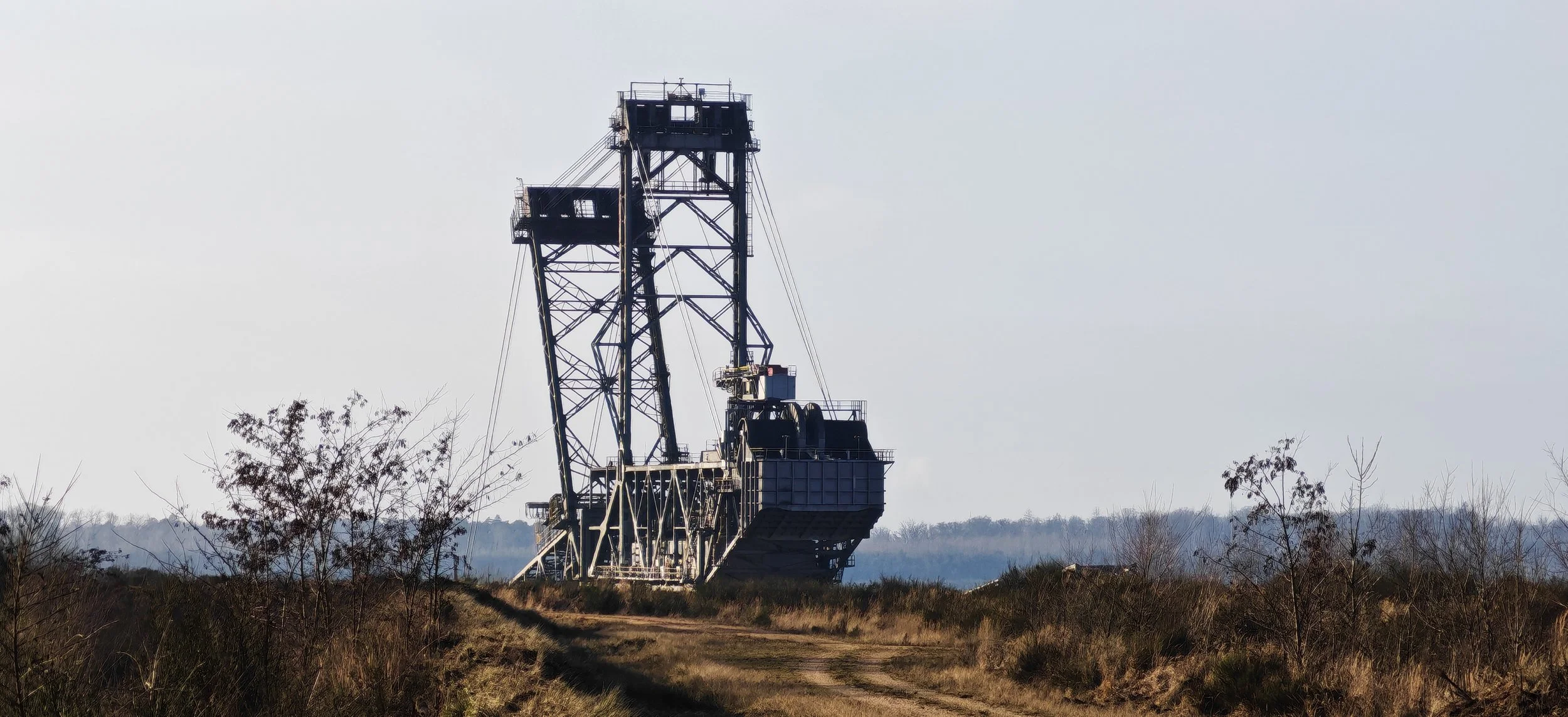 Rostförderturm in einer offenen Landschaft mit Büschen und Wegen, bei bewölktem Himmel.