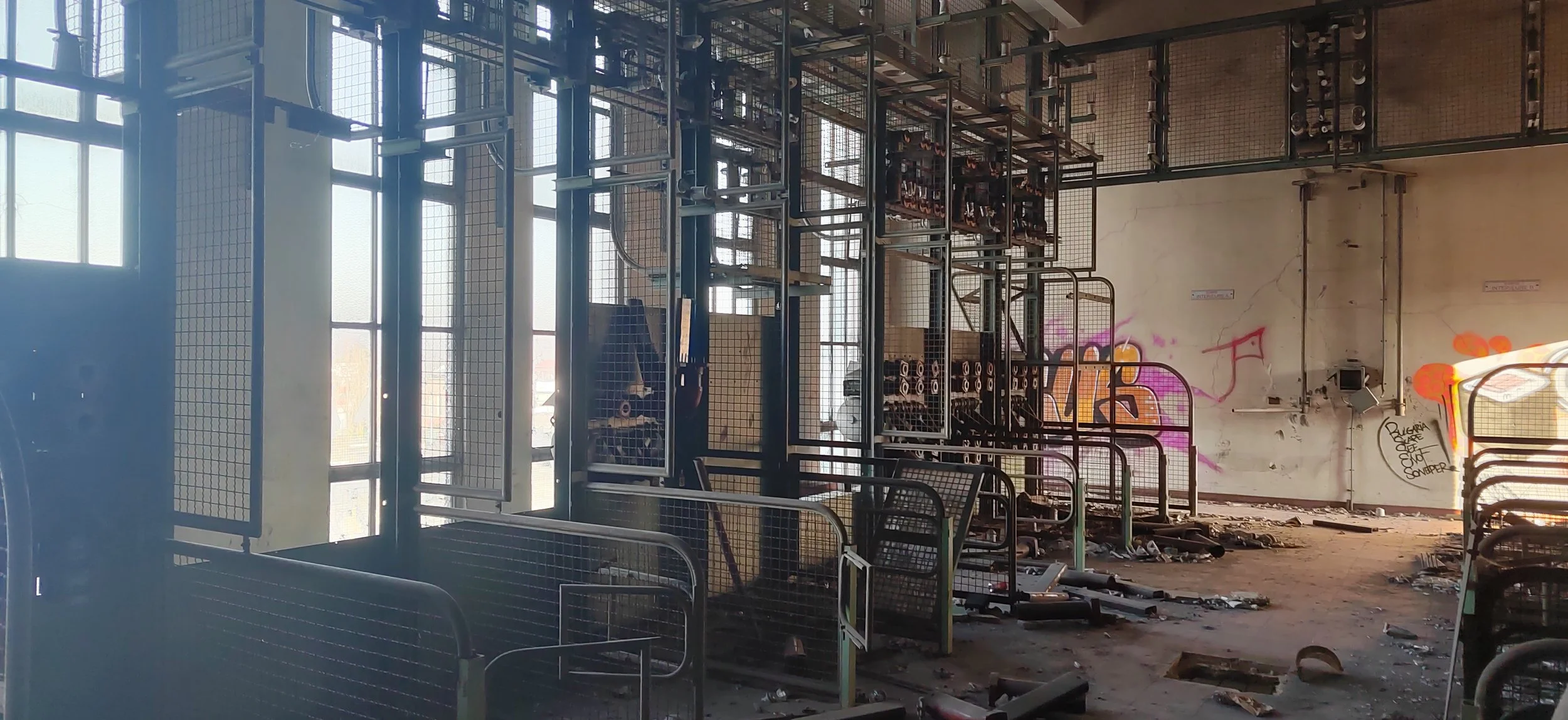 Innenraum eines verlassenen, verfallenen Gebäudes mit gestapelten Einkaufswagen, zerbrochenem Boden und Graffiti an der Wand.