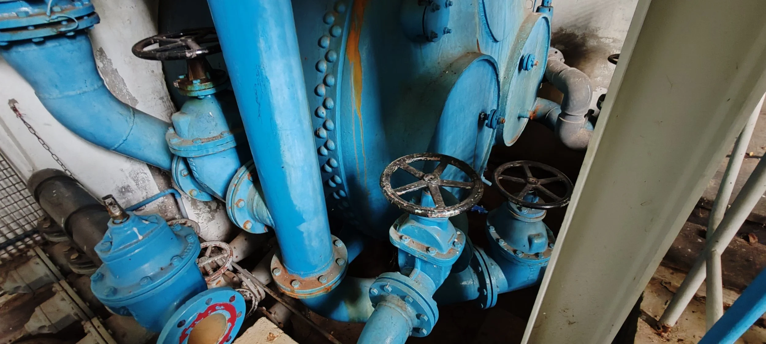 Blaue industrielle Rohre und Ventile in einem technischen Raum, einige sehen rostig und abgenutzt aus.