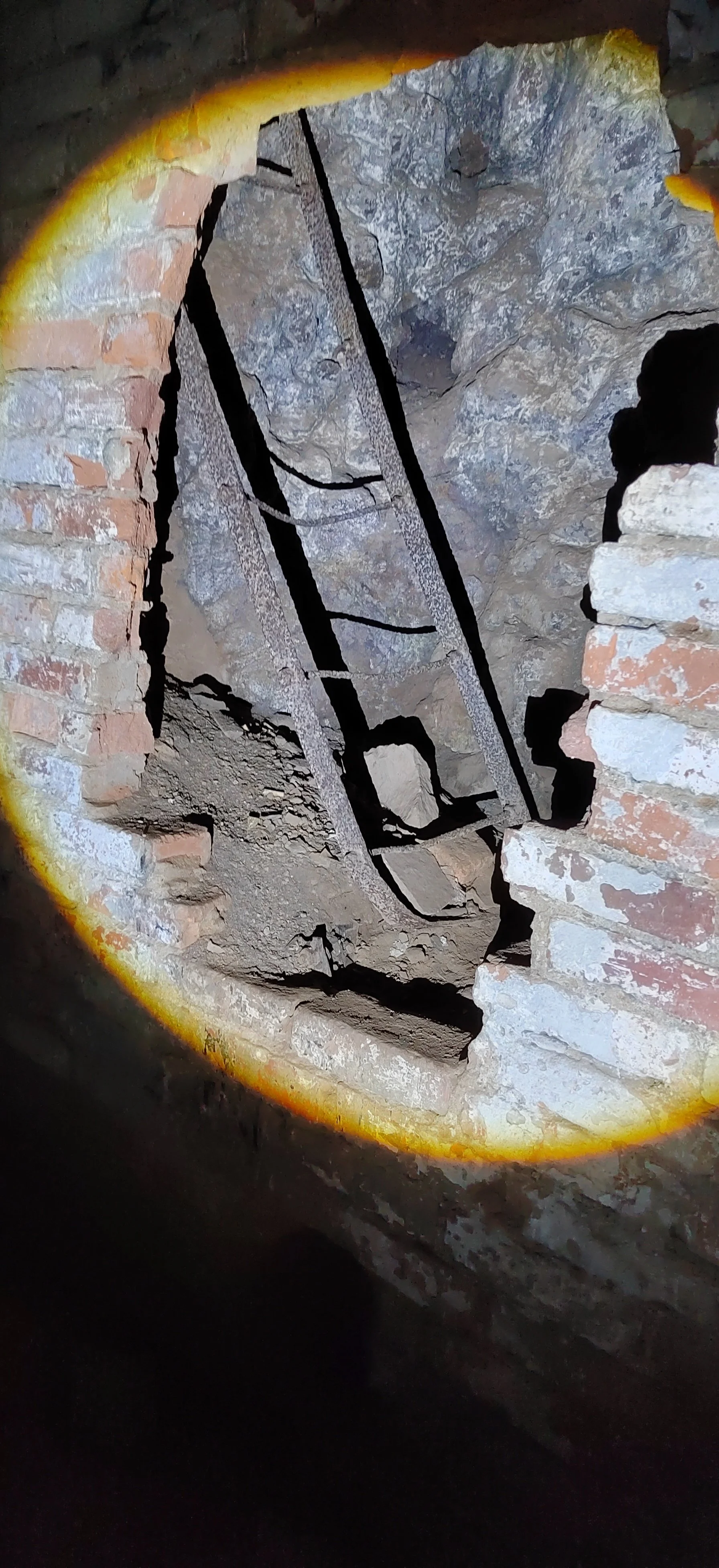 Fotografie einer alten, zerbrochenen Wand aus Backstein und Mauerwerk mit einem großen Loch, in das Licht fällt, umrahmt von einem gelben Kreis.