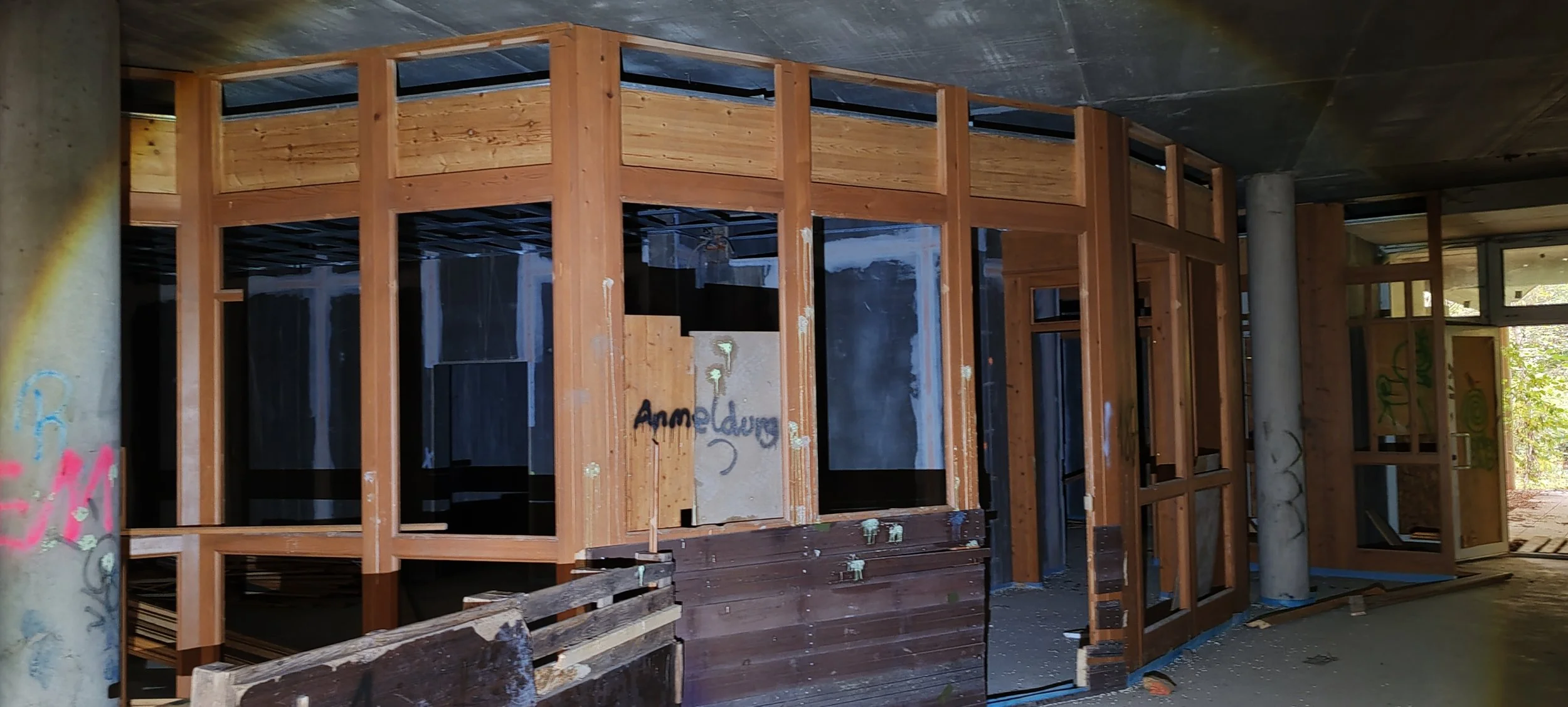 Innenaufnahme eines im Bau befindlichen Gebäudes mit Holzrahmen, Betonstütpfeilern und unvollendeten Wänden. Es sind Baugerüste und Baumaterialien sichtbar.