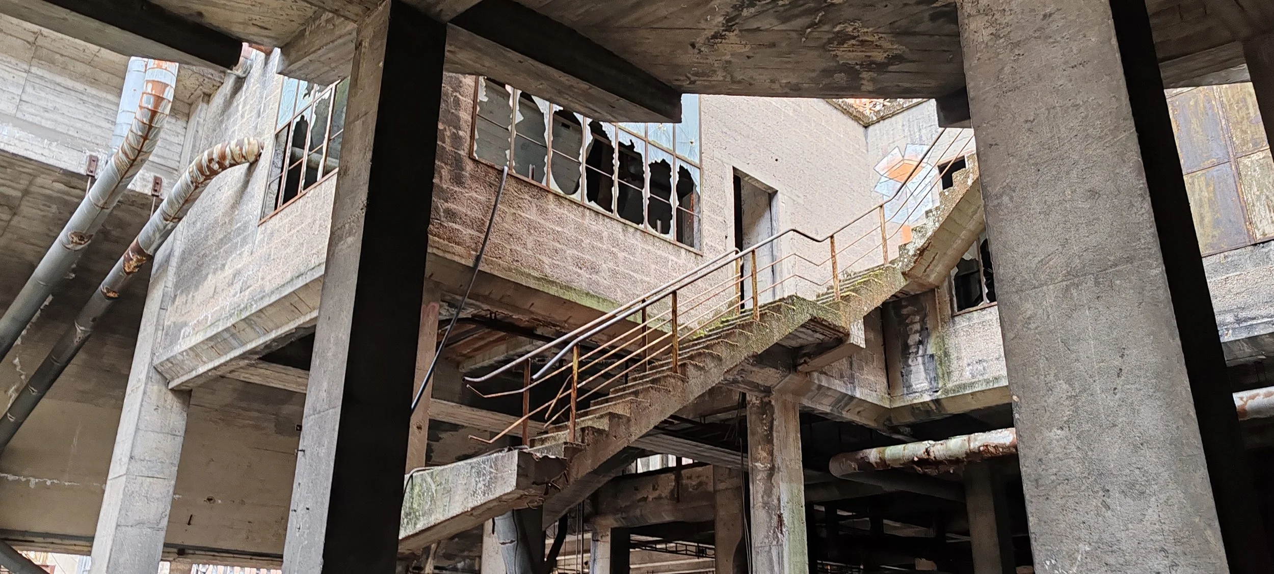 Verfallenes Gebäude mit zerbrochenen Fenstern, rostigen Außenbahn und unvollständiger Struktur, sichtbar von unten aufgenommen.
