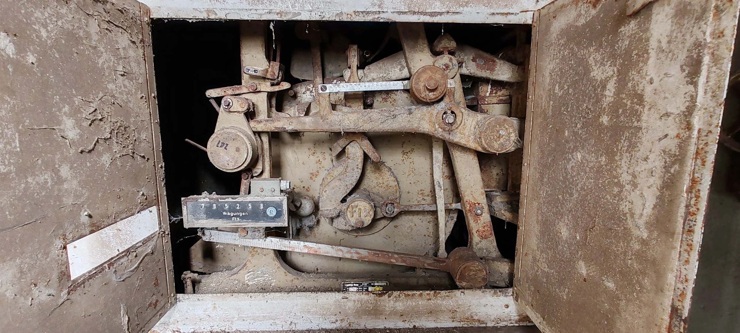 Alter Mechanismus mit verrosteten Teilen und einer Skala, vermutlich Teil einer Maschine oder eines Uhrenwerks.