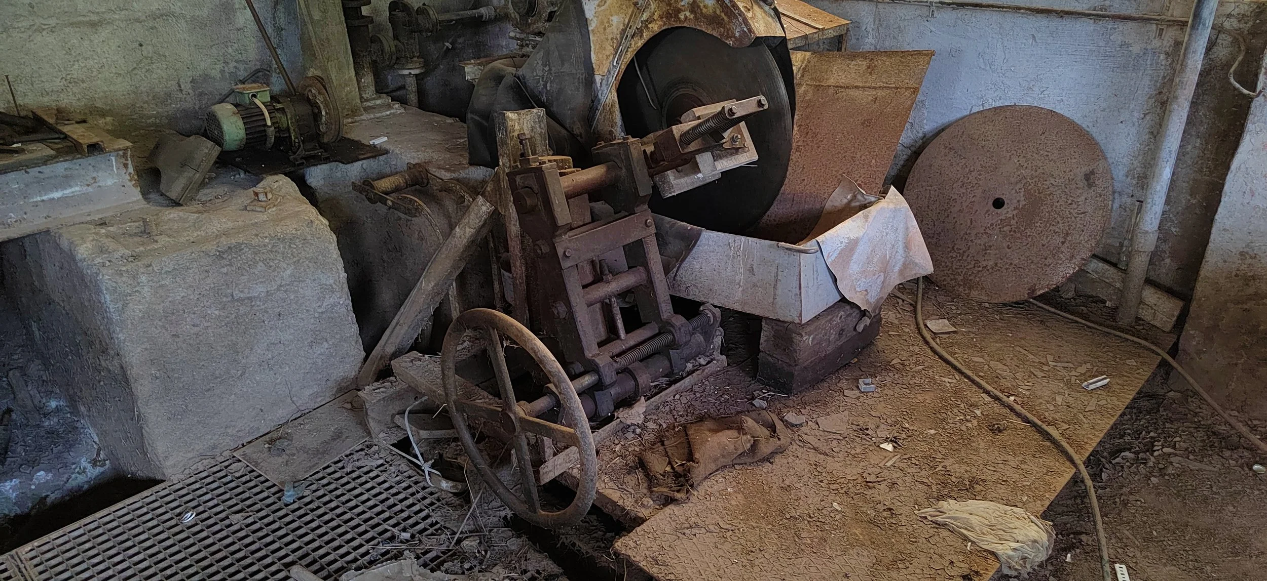 Ein alter, verstauberter Industrie-Rundschneider in einer Werkstatt mit Staub, Werkzeugen und zerbrochenen Gegenständen.