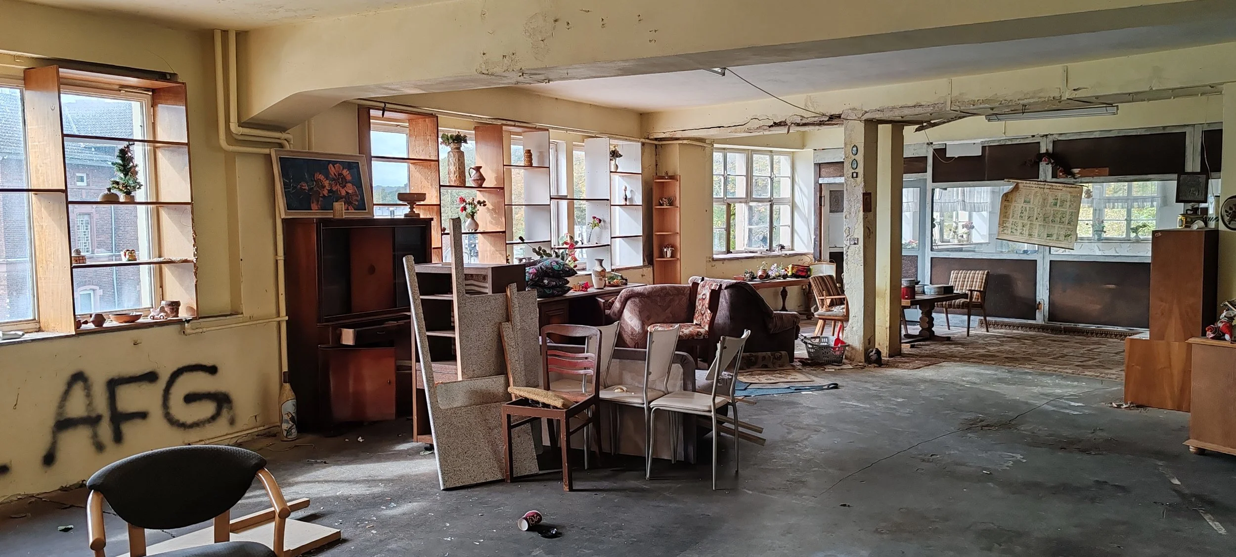 Ein verrauchtes, unordentliches Wohnzimmer mit zerbrochenen Fenstern und Möbeln, beschädigten Wänden und Graffiti auf der Wand.