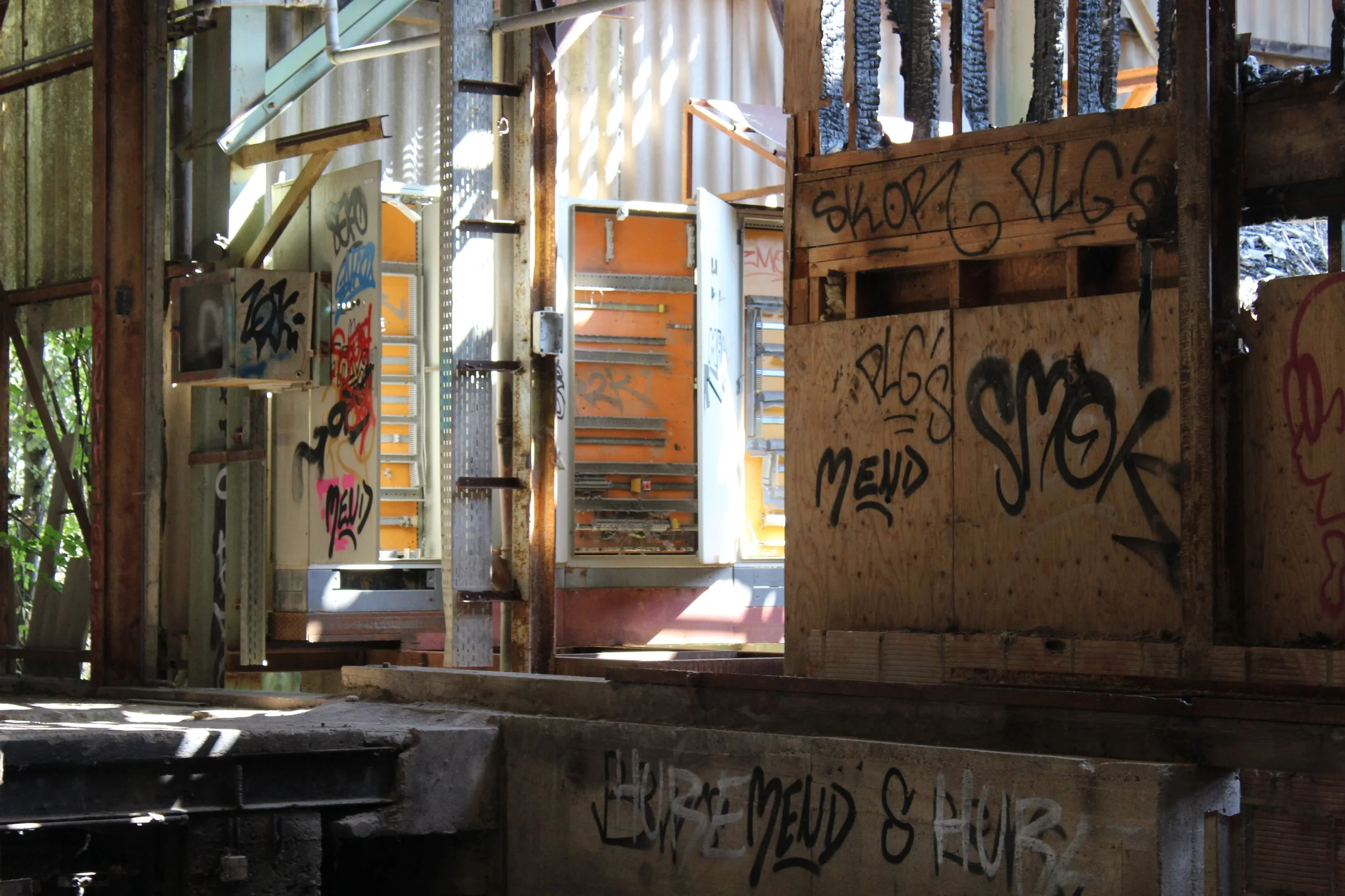 Ein verlassener, graffiti-beschmierter Bau im Innern mit Holz- und Metallteilen, getragen von einem Holz- und Stahlrahmen, mit Lichtstrahlen, die durch Ritzen in der Wand fallen.