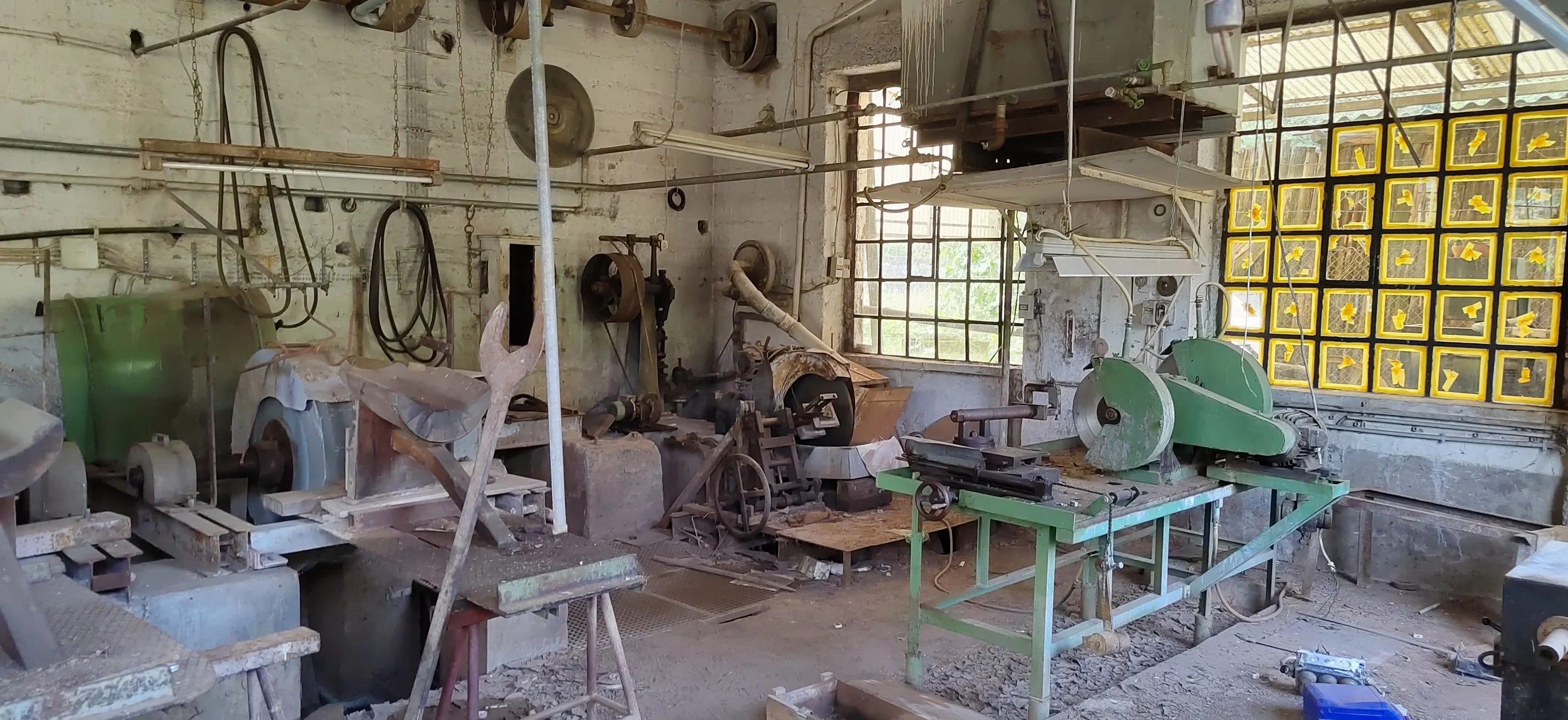 Ein alter, verlassener Maschinenraum mit verschiedenen Werkzeugen, Maschinen und Werkbänken, teilweise verschmutzt und staubig.