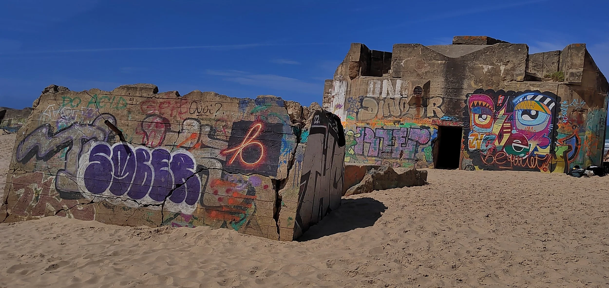 Verfallene Gebäudestruktur mit Graffiti an der Strandpromenade unter blauem Himmel.