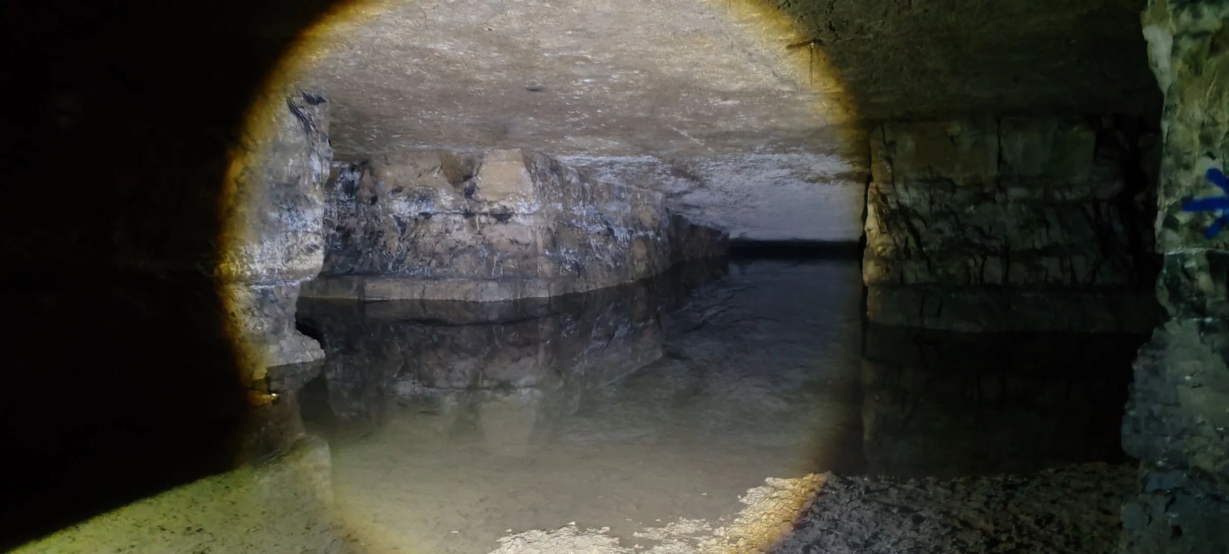 Höhleninneres mit Wasser und Felsformationen, beleuchtet mit Taschenlampe, Reflexionen im Wasser