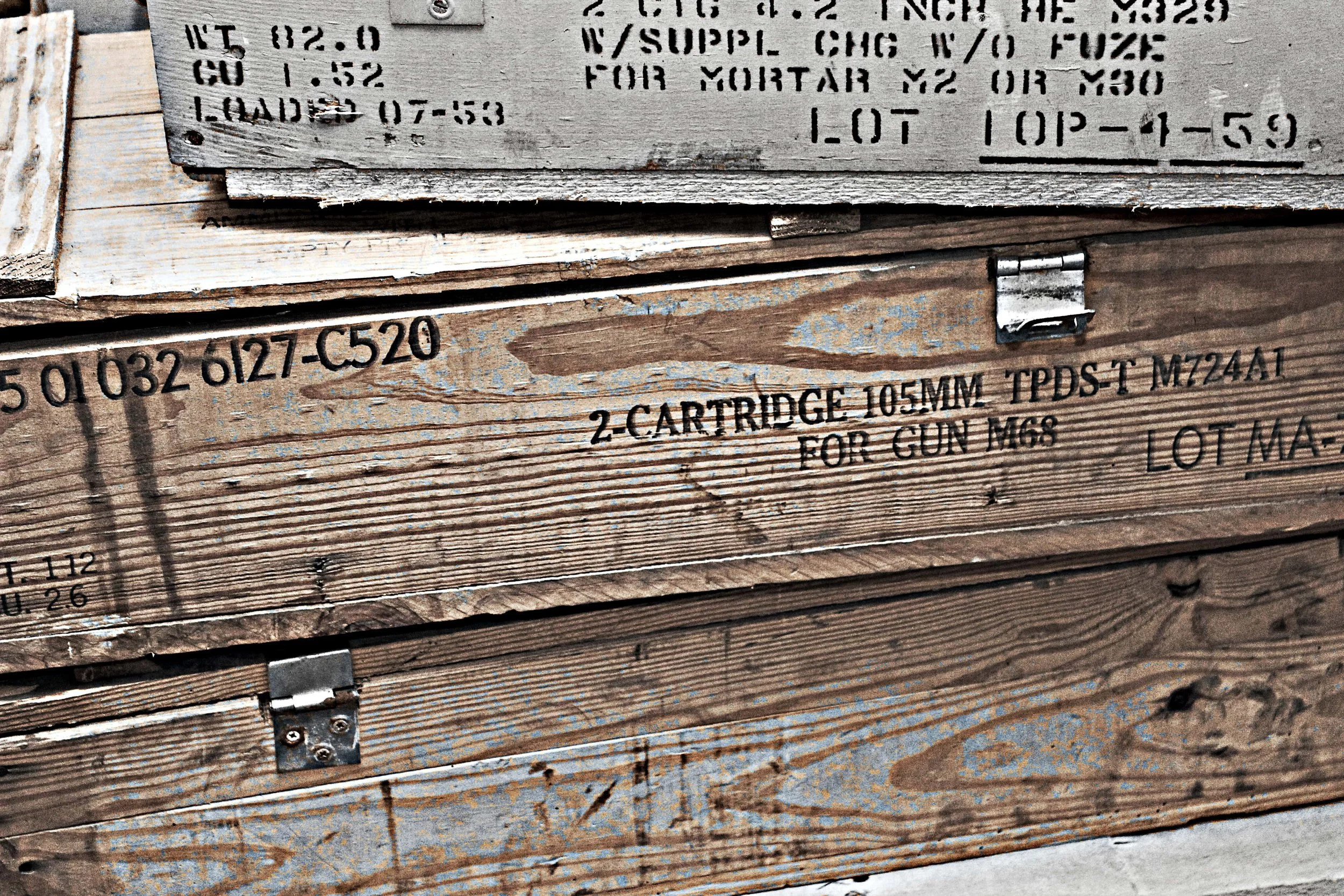 Holzkisten mit aufgedruckten Etiketten und Beschriftungen, die Munition und Waffenzubehör enthalten.