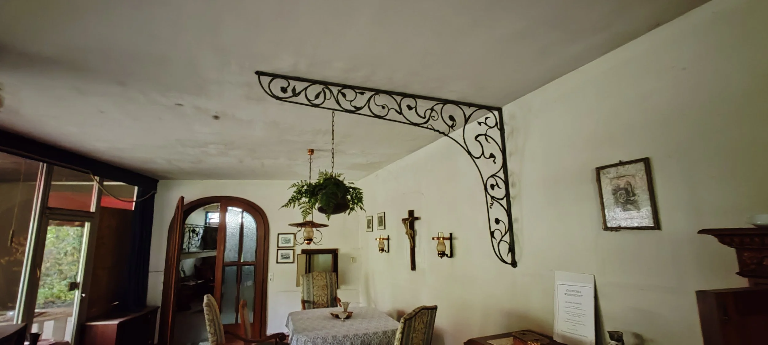 Innenraum eines Wohnzimmers mit hängender Pflanze, antiken Möbeln, Wanddekorationen und einem Esstisch.