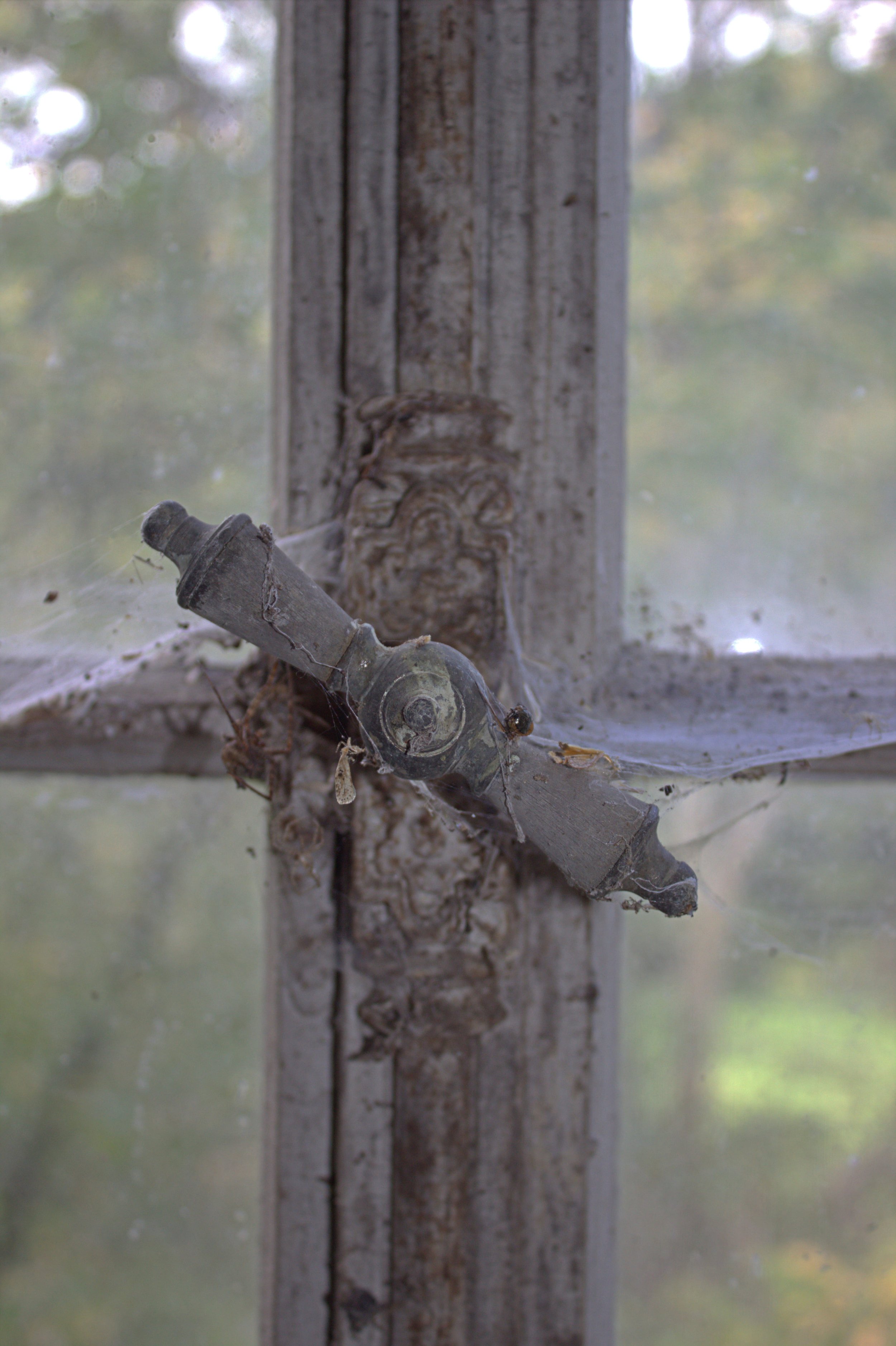 Alte, verrostete Fensterbeschlag an einem holzverkleideten Fensterrahmen, mit Staub und Spinnweben bedeckt.