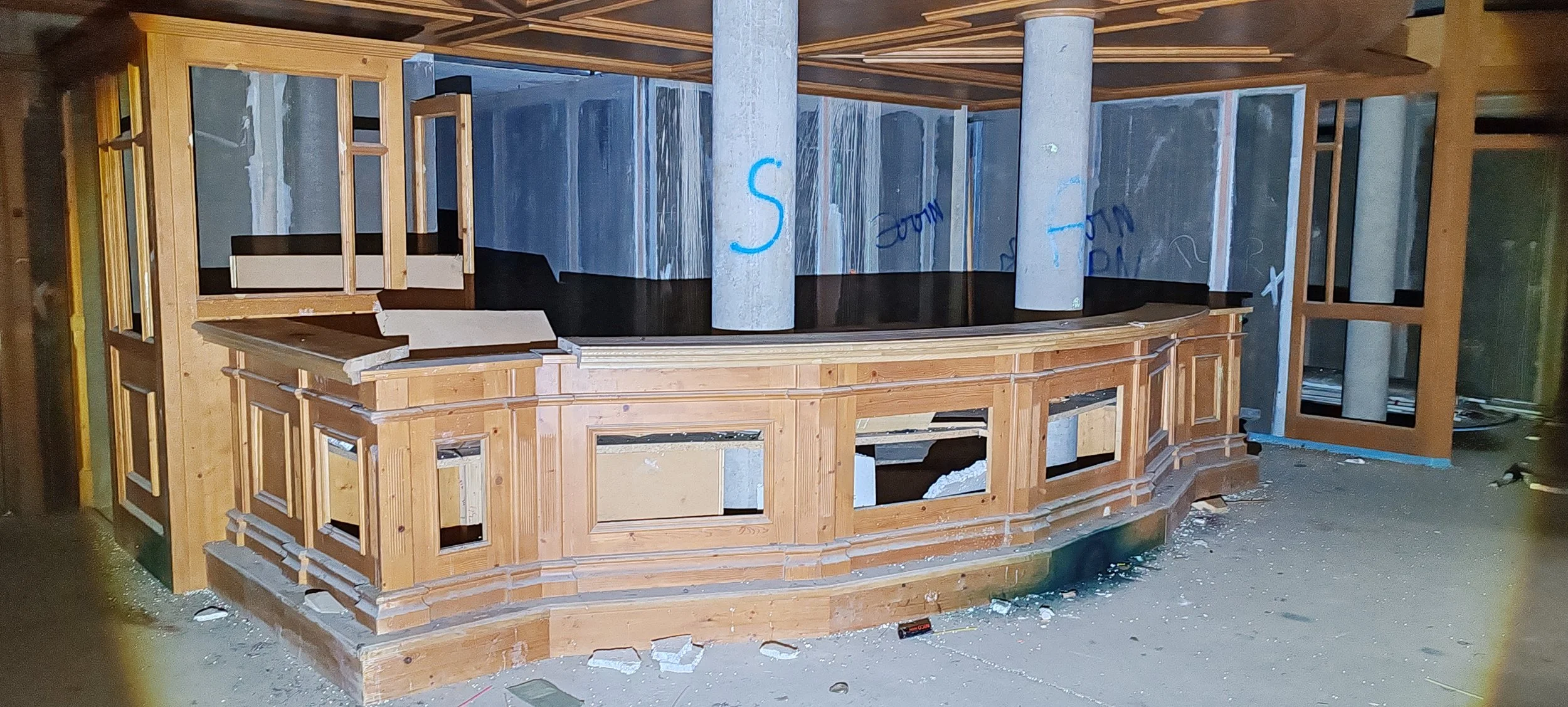 Holzbar, die noch im Bau ist, mit einem halb runden Tresen, bestehend aus Holzrahmen und schwarzen Oberflächen, in einem Raum mit Betonwänden und Säulen, Baumaterialien und Werkzeug liegen auf dem Boden.