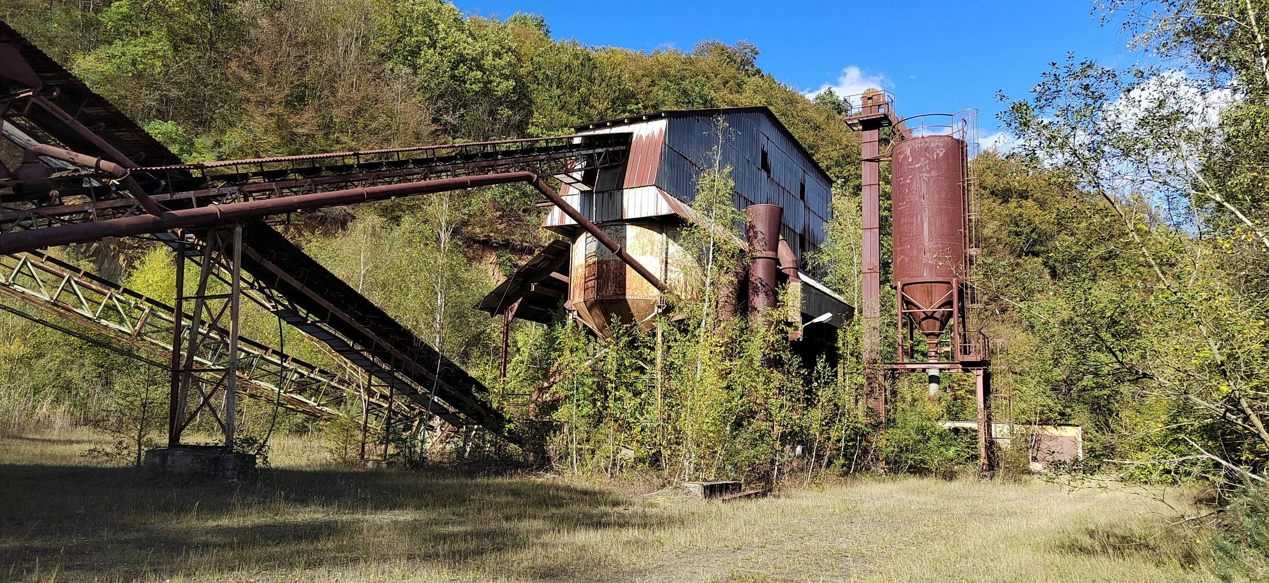 Verrostete alte Industriemaschine inmitten von Bäumen auf einer Wiese, blauer Himmel