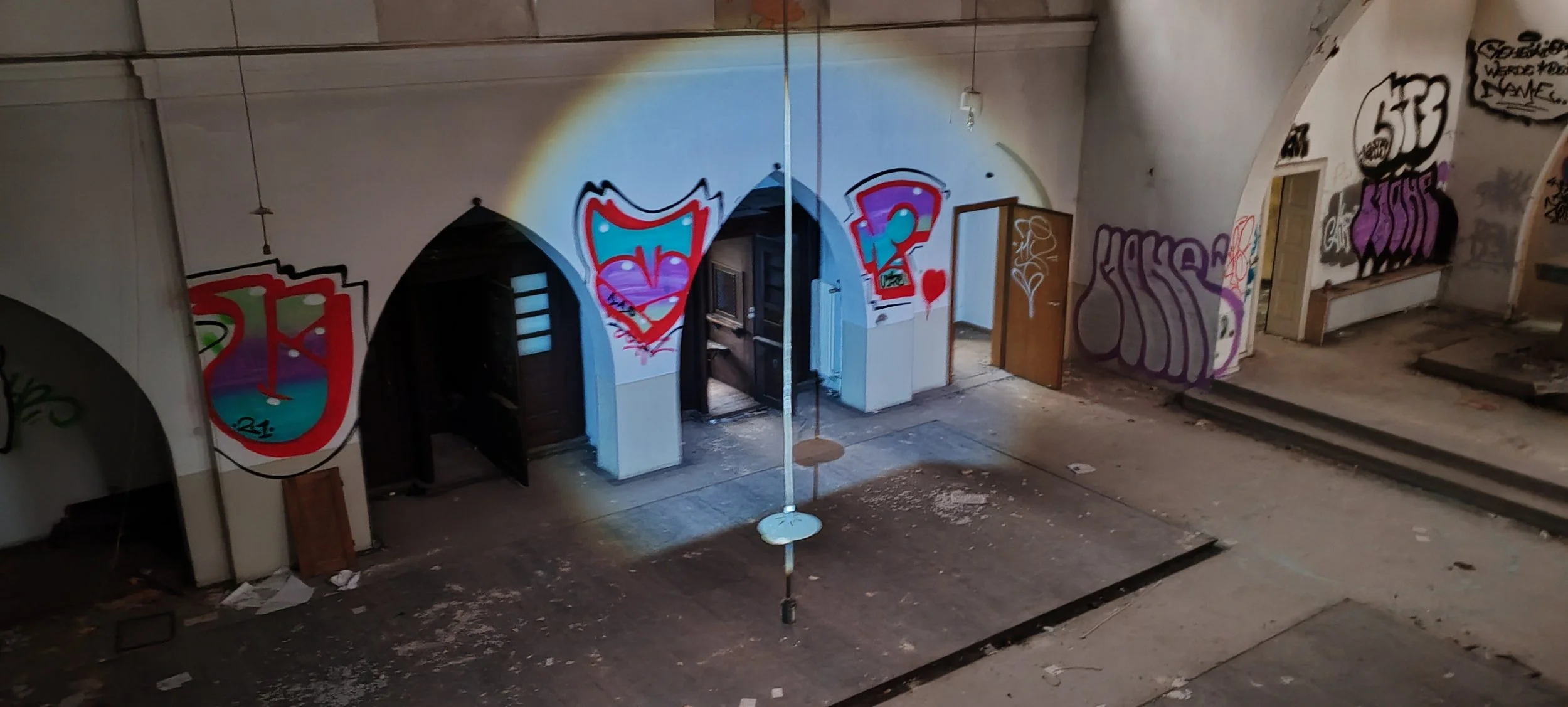 Innenansicht eines verlassenen, mit Graffiti bedeckten Raums, mit schmutzigen Böden, offenen Türen und einer Balanceleine in der Mitte, die an einem Fliegengewicht hängt.