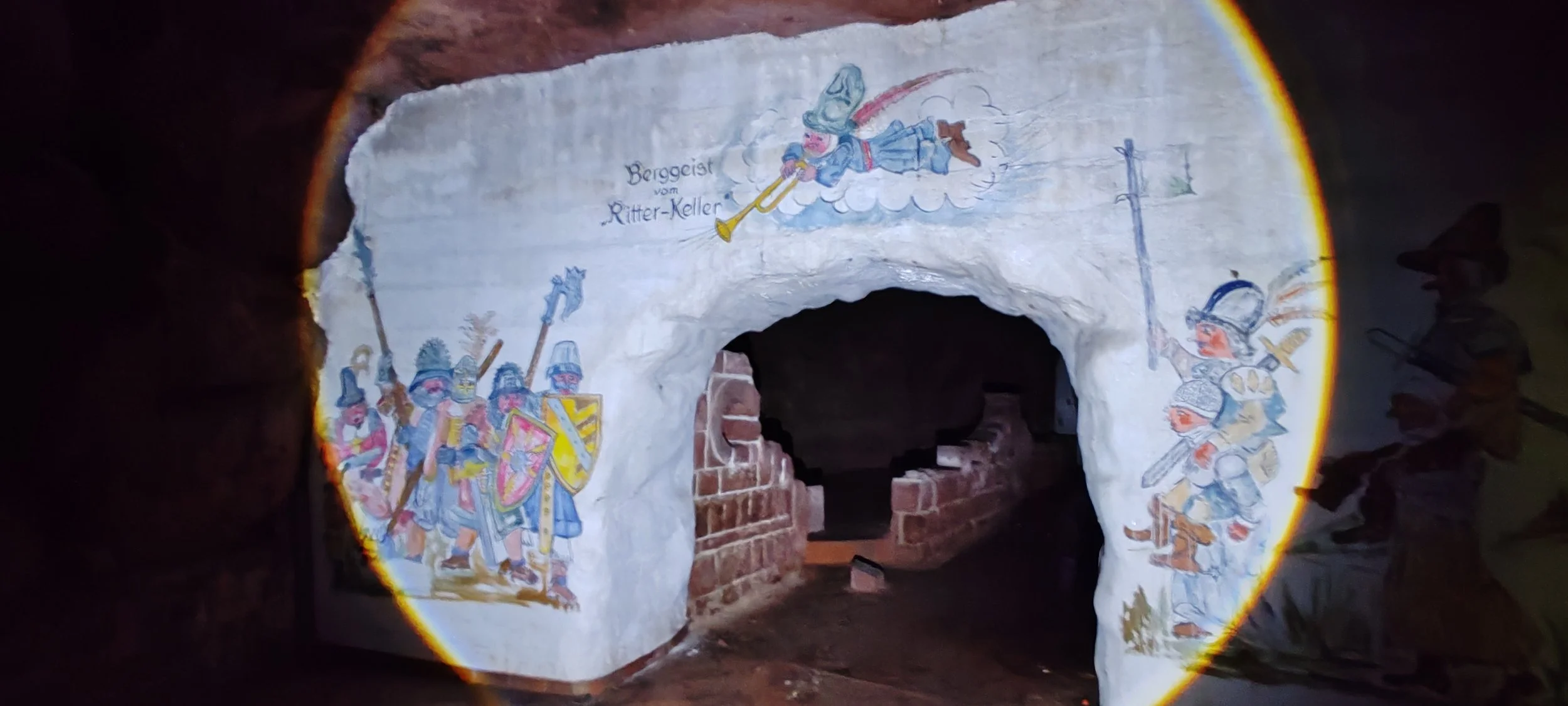 Fresko an einer Wand zeigt Ritter in mittelalterlicher Rüstung und bewaffnet, mit einem Ritter in der Mitte der auf einer Wolke schwebt und ein Horn bläst, mit dem Titel 'Bergeist vom Ritter-Keller'.