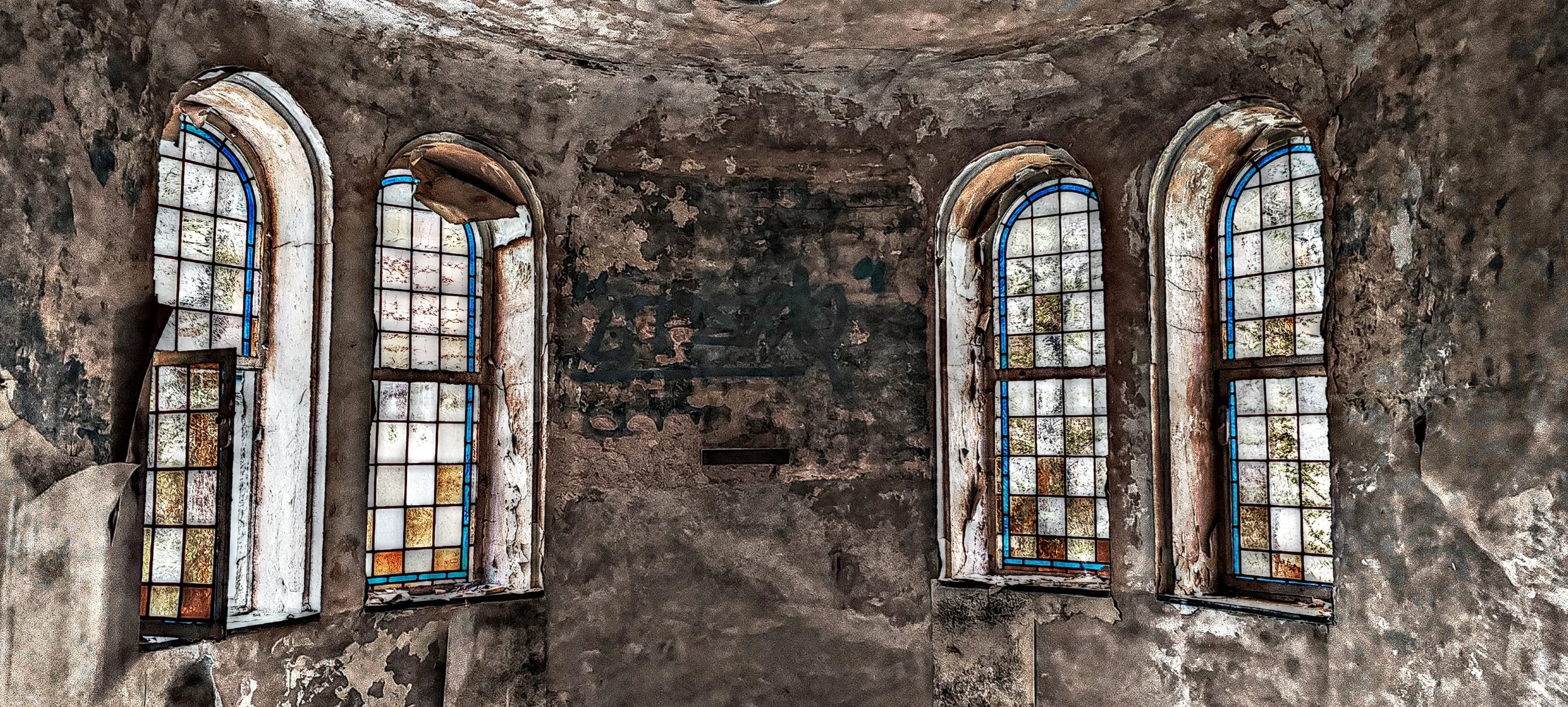 Vier alte, bunte Kirchenfenster in eine beschädigte, verfallene Wand eingebaut.