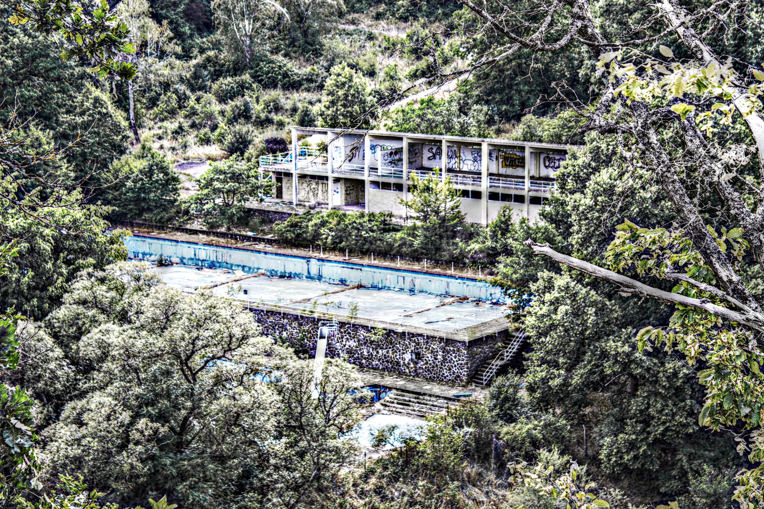 Verfallene, leerstehende Gebäude inmitten dichtem, grünem Wald mit Graffiti an den Wänden.