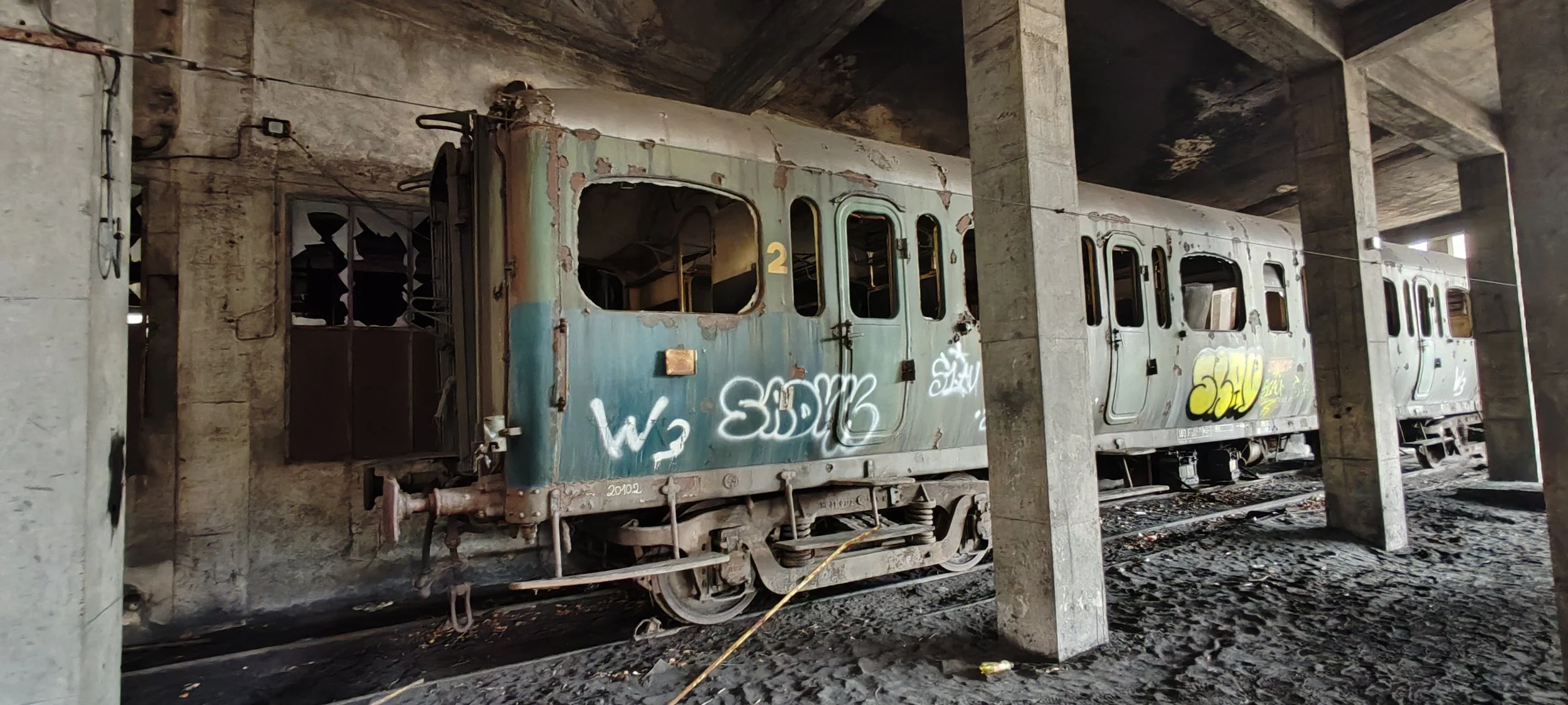 Verrosteter und verlassener Eisenbahnwagen mit Graffiti auf einer Schiene, in einer alten Tunnelstruktur
