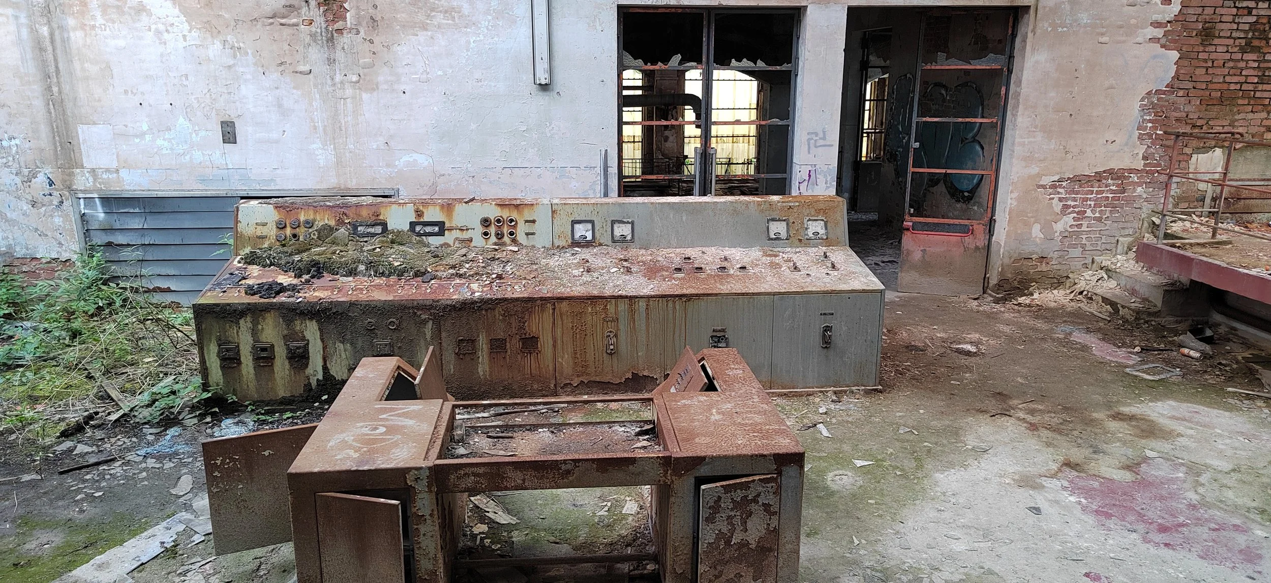 Verbrannte und verfallene Elektronikstation in einem verlassenen und zerstörten Gebäude, mit verfaulten Wänden und vergitterten Fenstern.