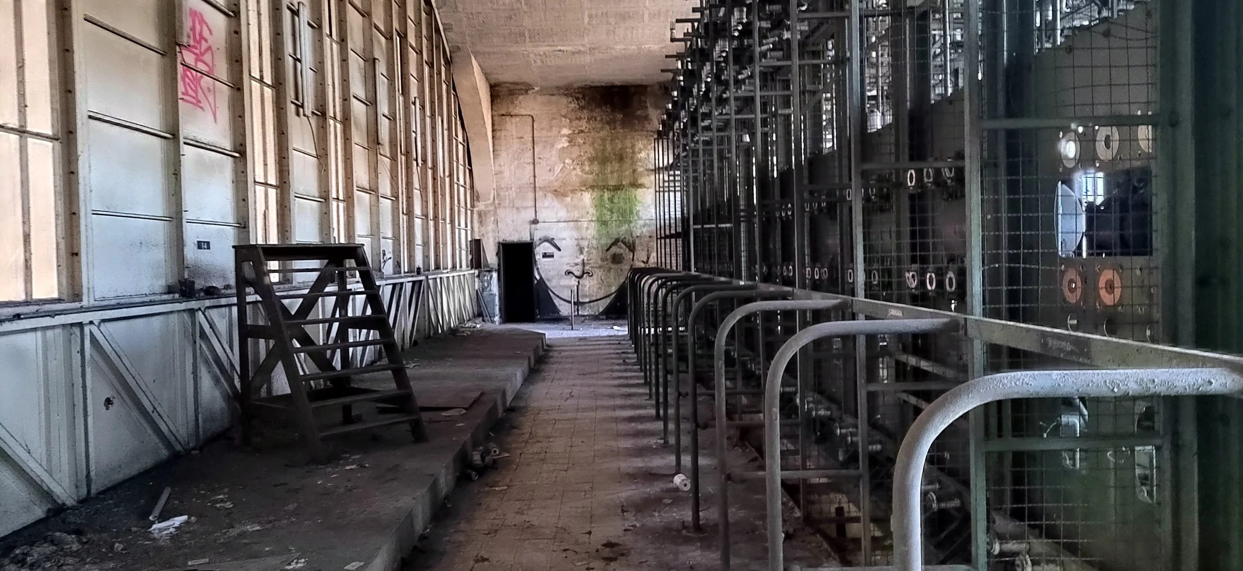 Ein verlassener, heruntergekommener Raum mit metallischen Gerüsten und einer unordentlichen, schmutzigen Bodenfläche, wahrscheinlich eine alte Fabrikhalle oder Lagerraum.
