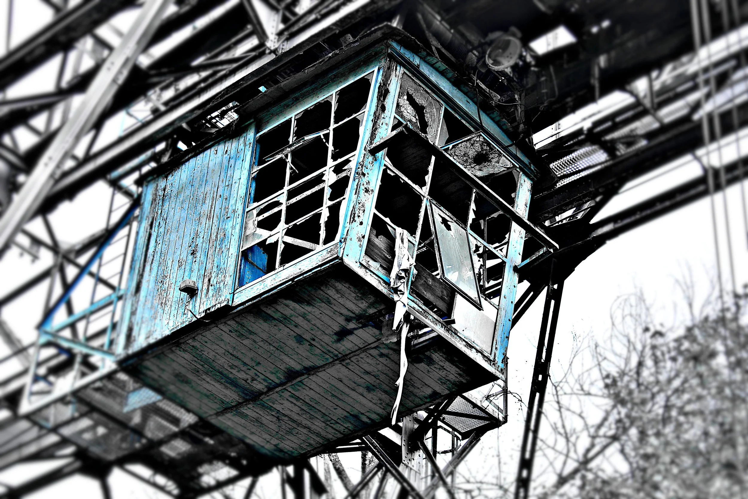 Verfallenes, blau gestrichenes Baumhaus an einer alten Turmkonstruktion, mit beschädigten Fenstern und kaputtem Holz, im Hintergrund ein winterliches, verschwommenes Baum.